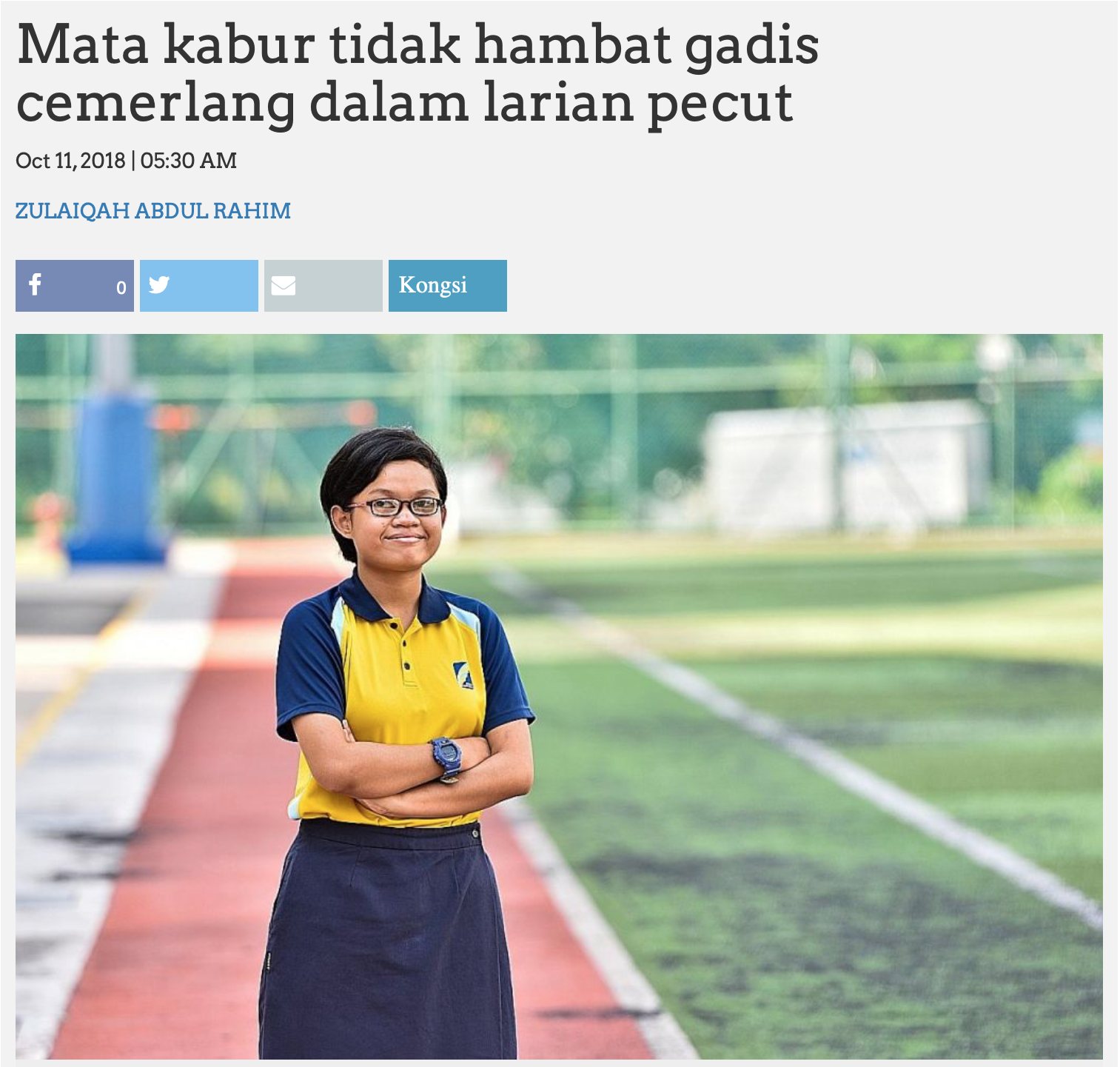 Young woman in glasses and yellow uniform stands arms crossed on a red running track beside a green field.