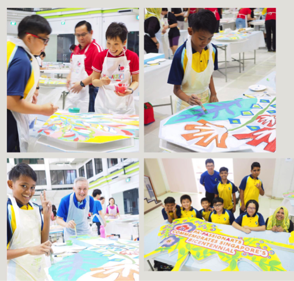 Children and adults in aprons painting a large colorful mural commemorating Singapore's Bicentennial.
