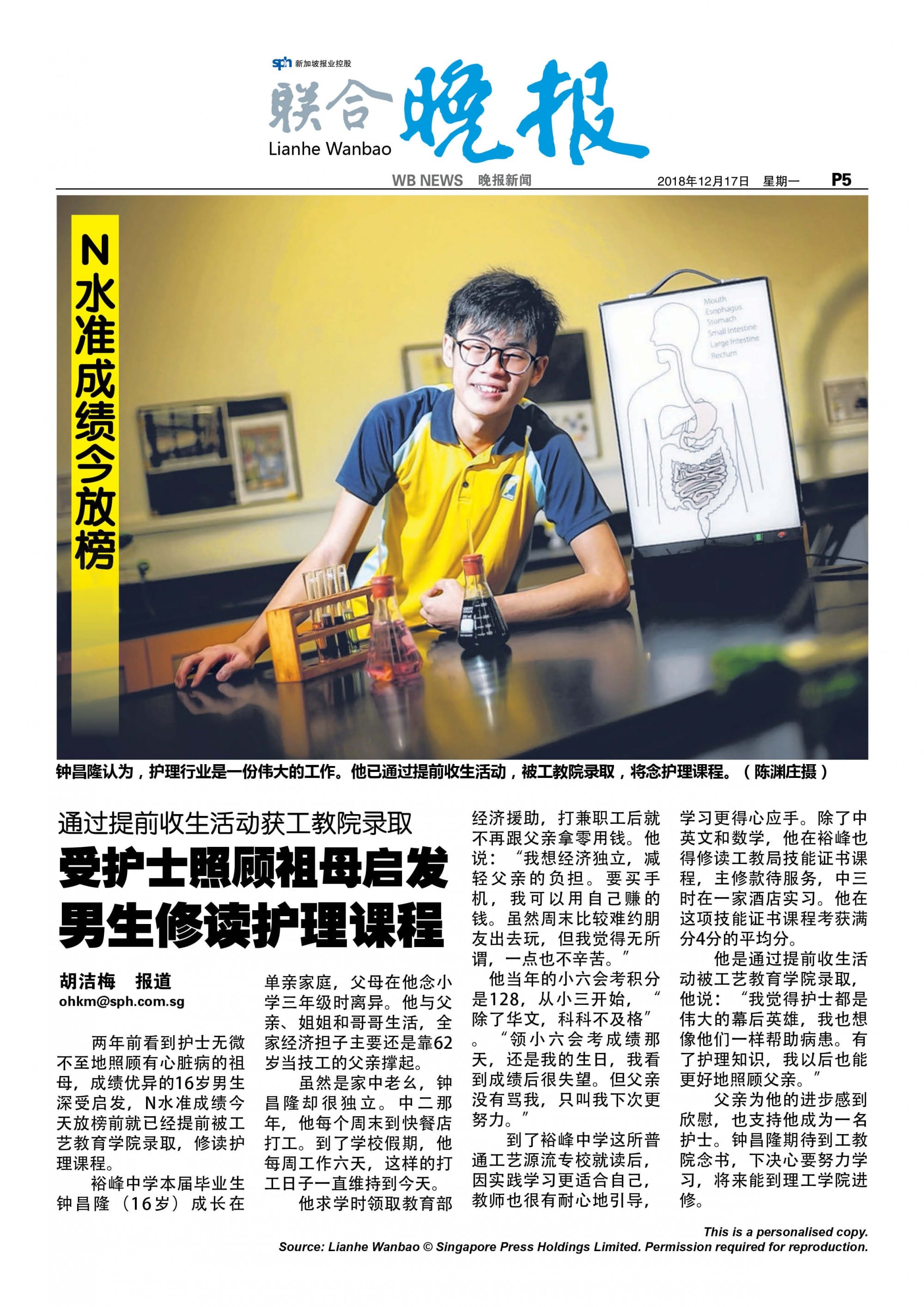 A smiling teenage boy in a yellow shirt sits at a desk with science equipment and a digestive system diagram behind him.