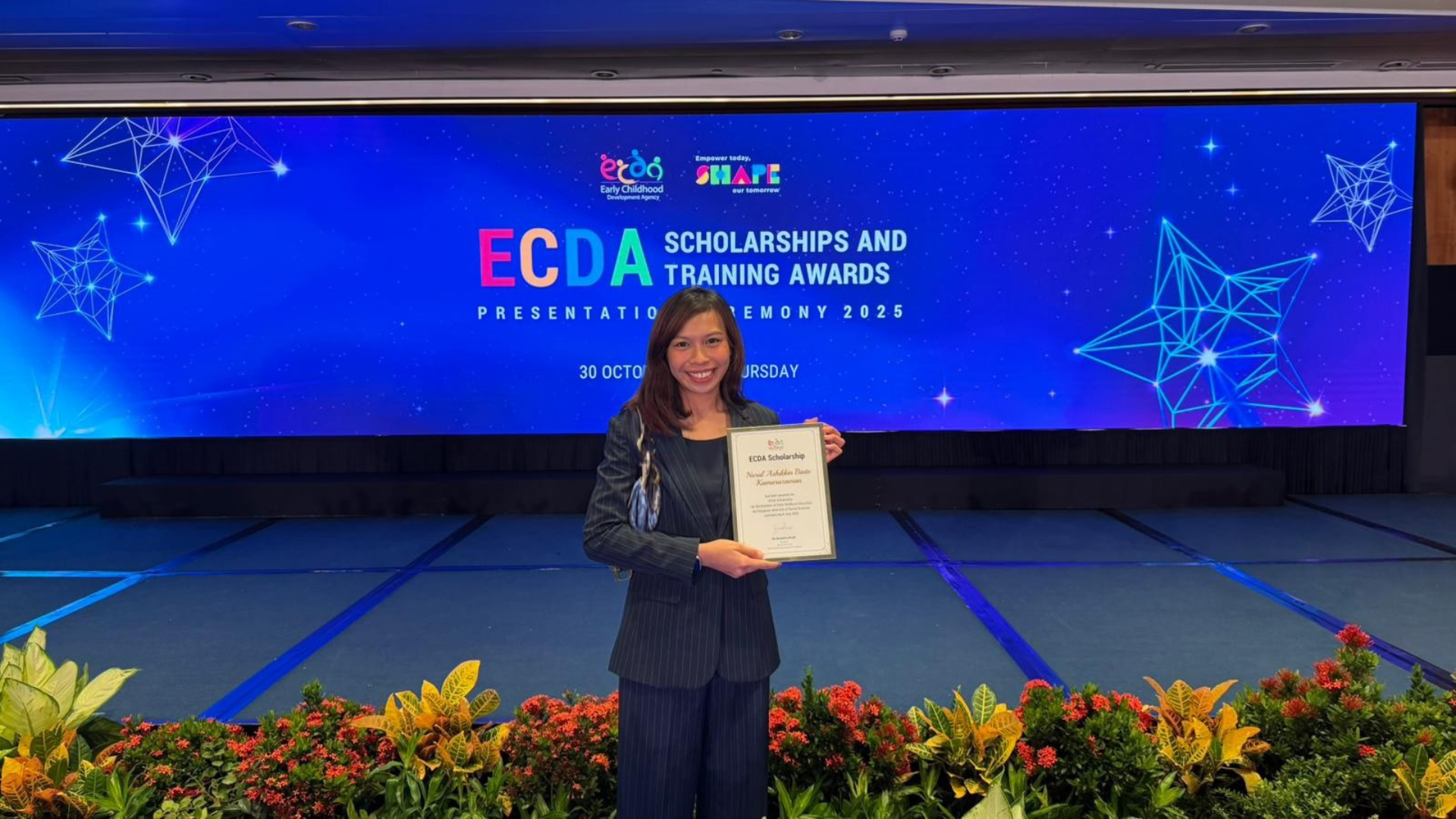 Ash holds an ECDA scholarship certificate in front of a blue ECDA Scholarships and Training Awards 2025 banner.