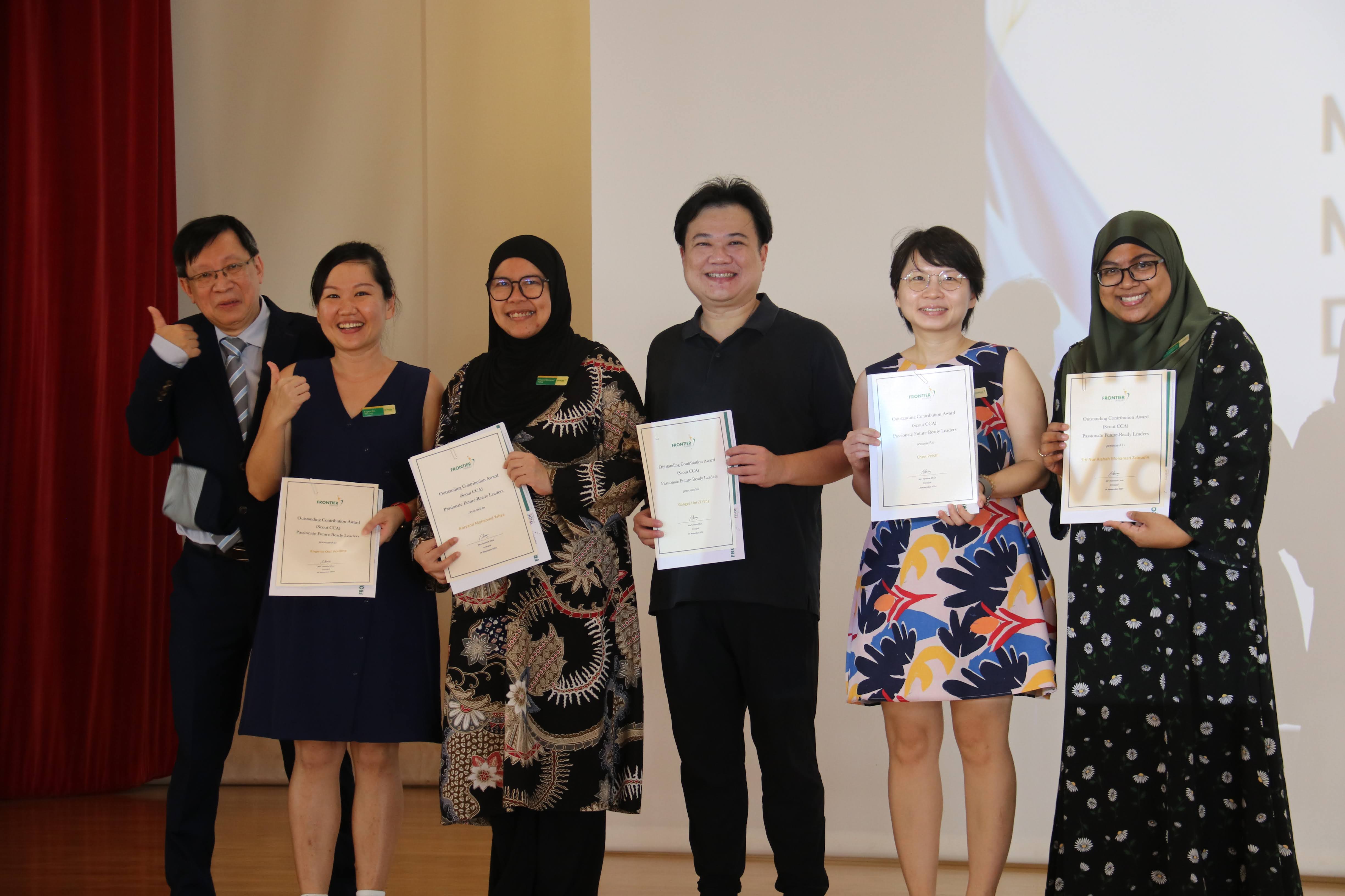 Six smiling people stand together, five holding award certificates, posing for a group photo indoors.