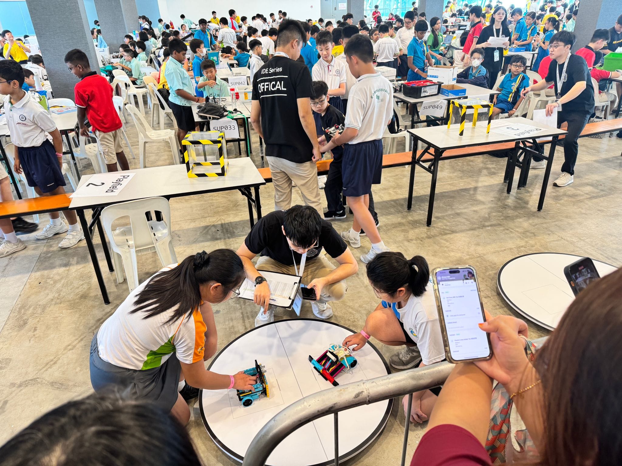 Students compete in a large robotics competition, testing small robots on circular tracks with an official observing.