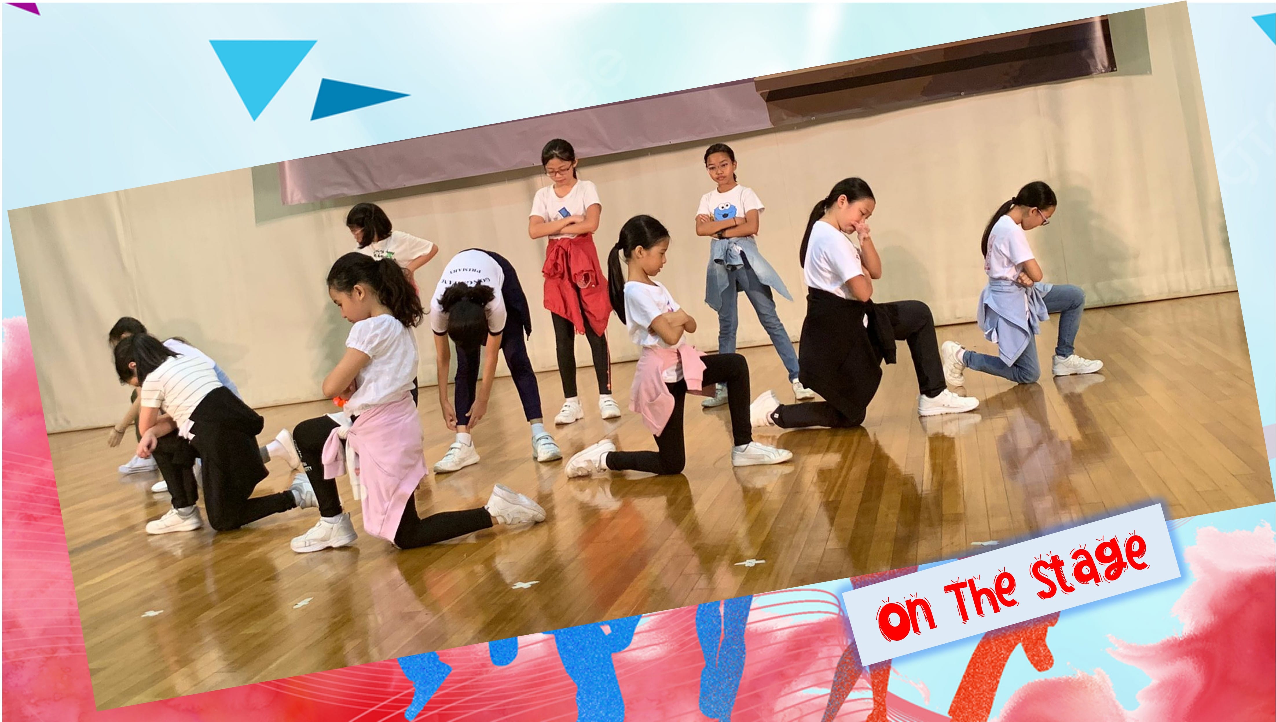 A group of young girls in white shirts perform a synchronized dance routine on a wooden stage floor.