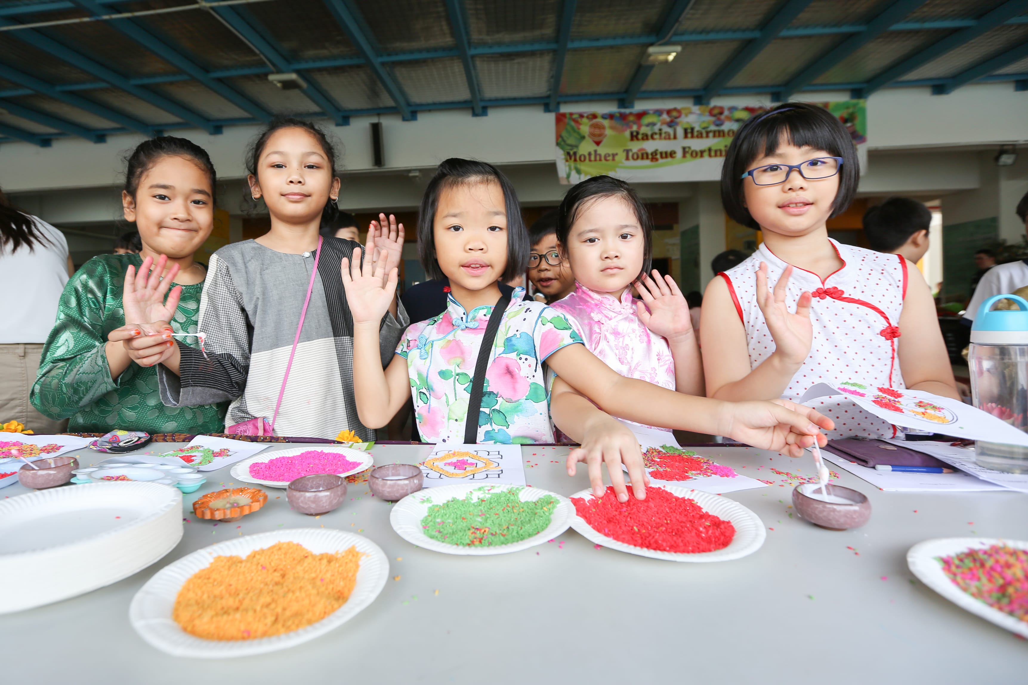 Five children wave behind a craft table with paper plates of colored sprinkles and small bowls.