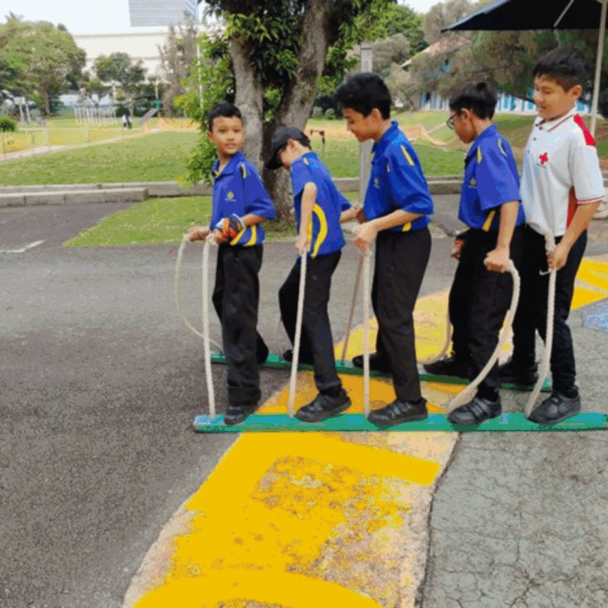 Five schoolboys in uniforms stand on long wooden boards with ropes, moving together outdoors.