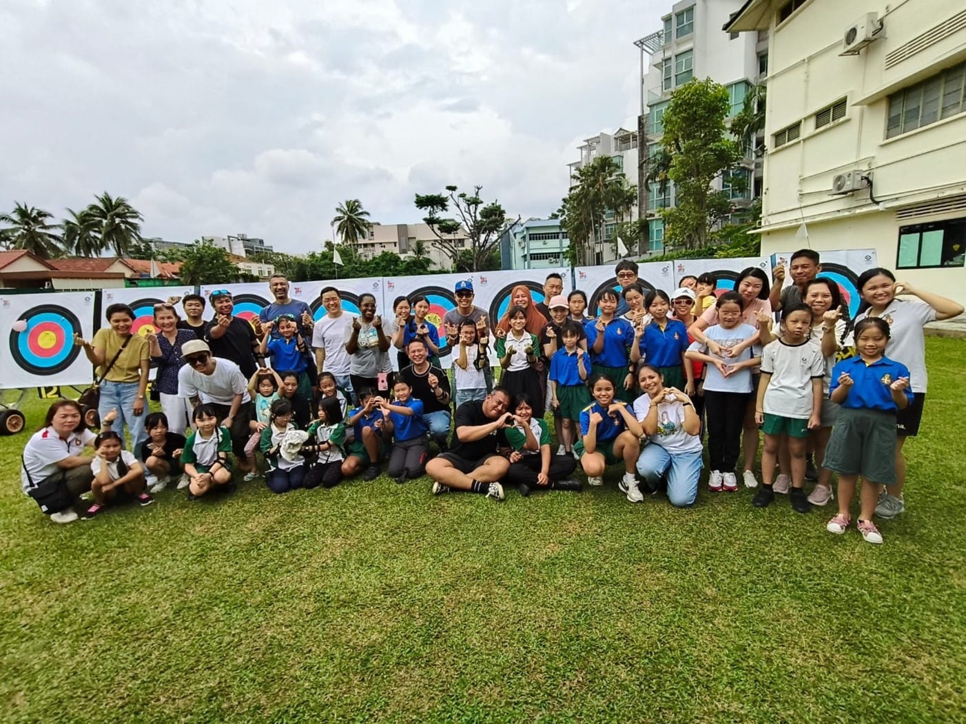 Large group of adults and children posing outdoors in front of colorful archery targets on a grass field.