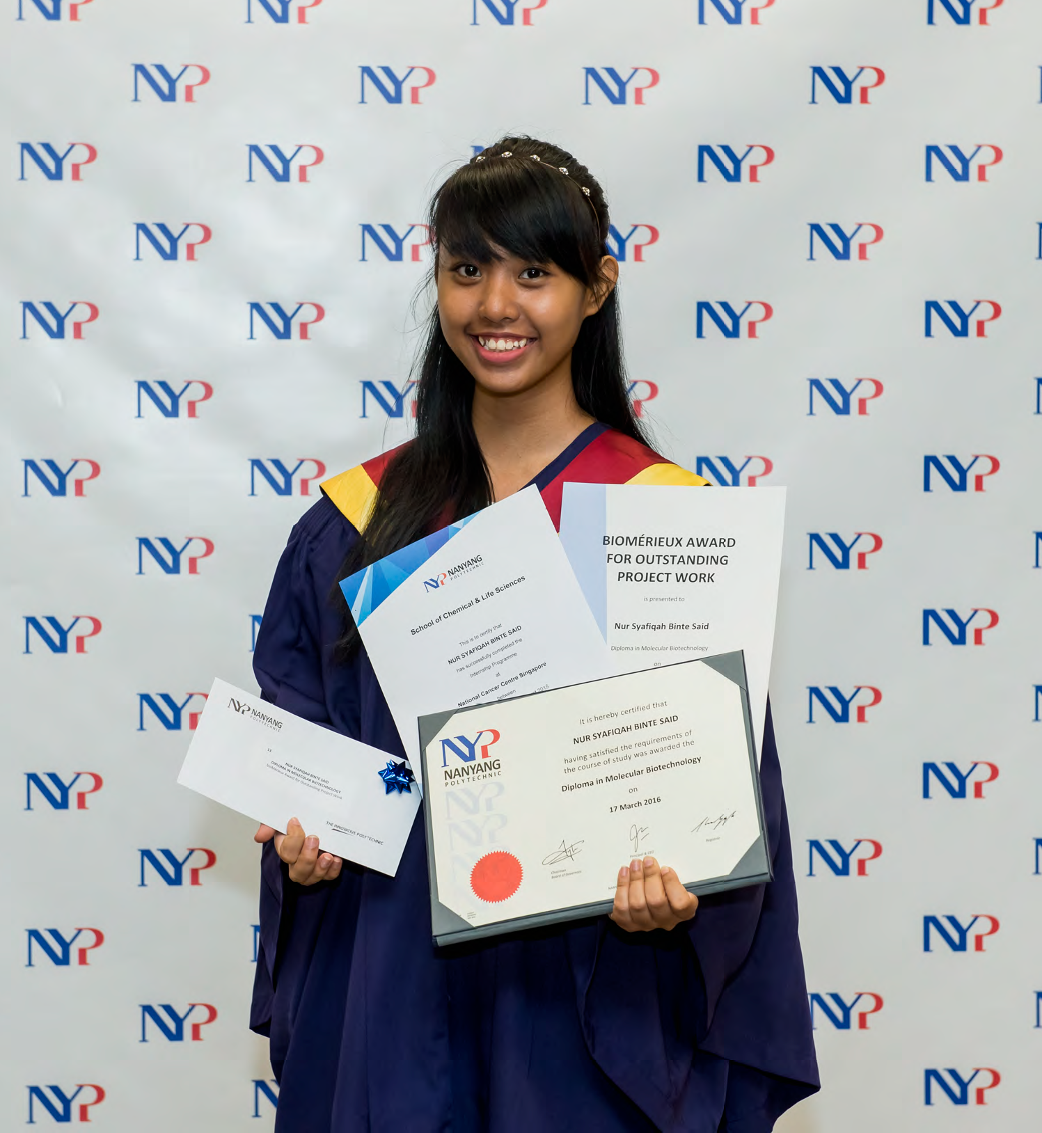 A smiling young woman in graduation gown holds a Nanyang Polytechnic diploma and a Biomerieux Outstanding Project Award certificate.