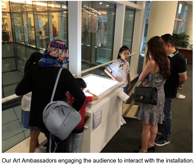 A young girl in a white uniform guides visitors at a bright interactive table in a modern building interior.
