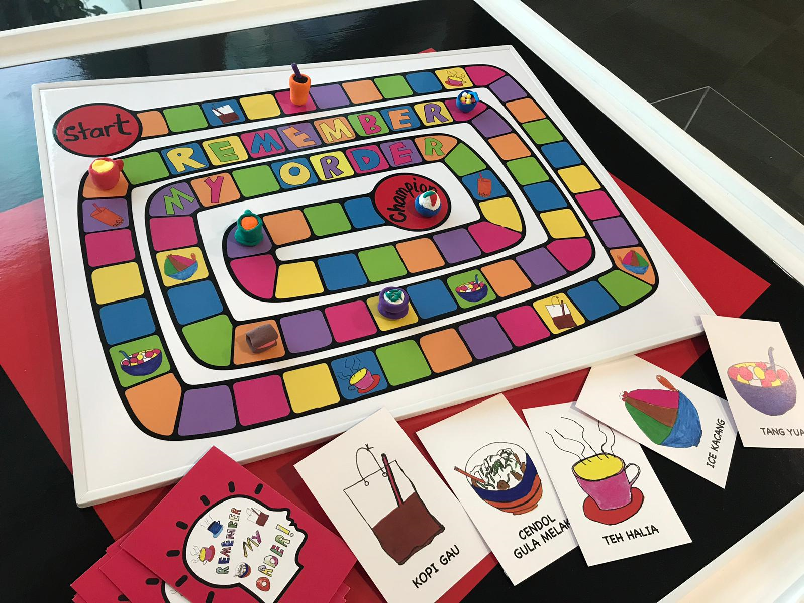 Colorful board game titled "Remember My Order" with food-themed cards showing drinks and desserts like Cendol and Teh Halia.