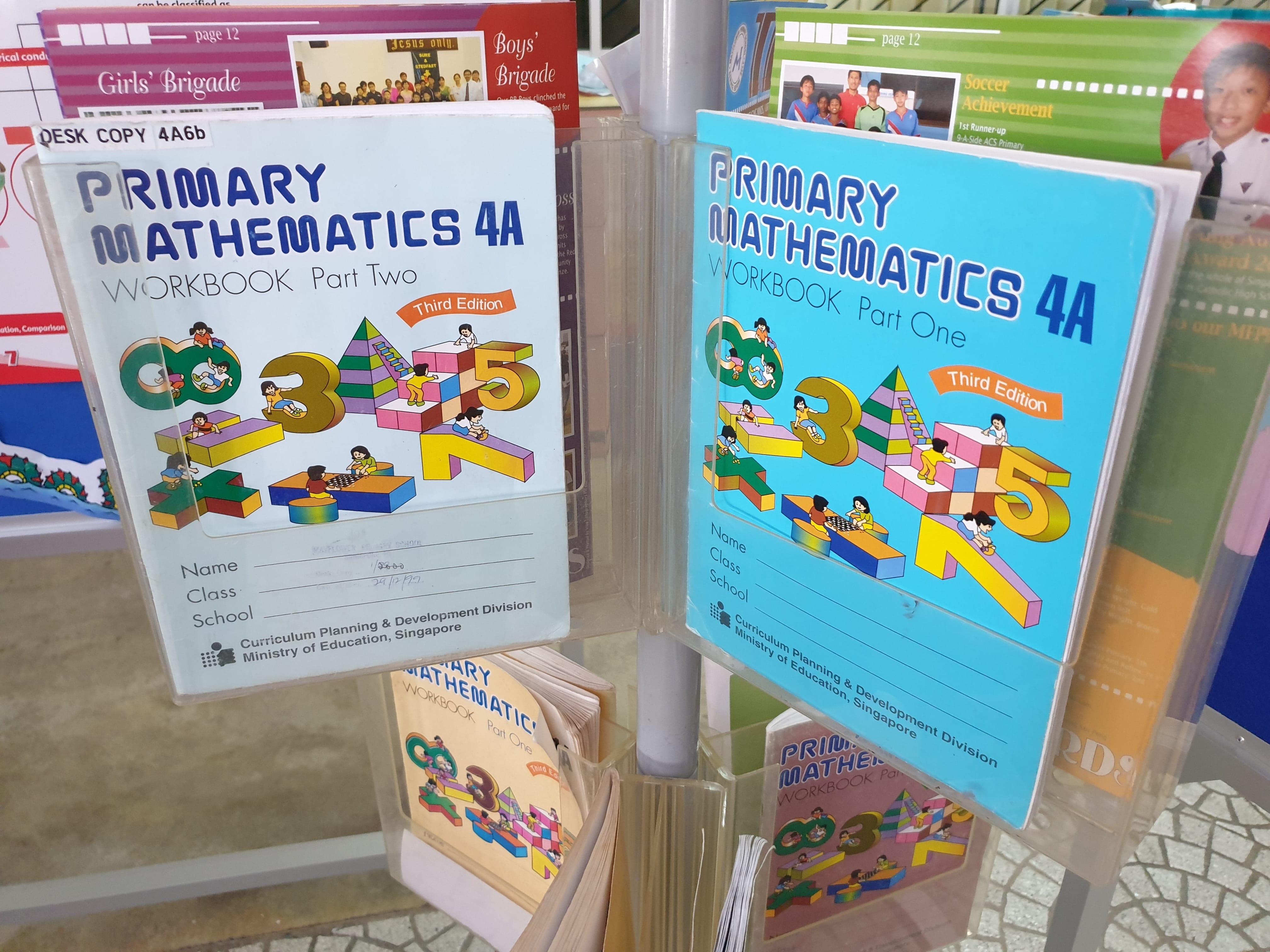 Two Primary Mathematics 4A workbooks, Part One and Part Two, Third Edition, displayed in a rack.