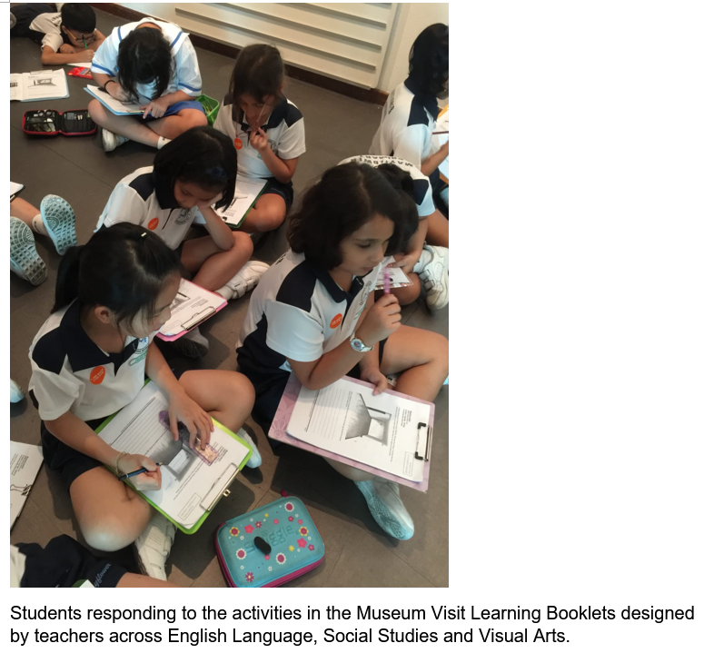 Several young students in school uniforms sit on the floor writing on clipboards with worksheets during a museum visit.