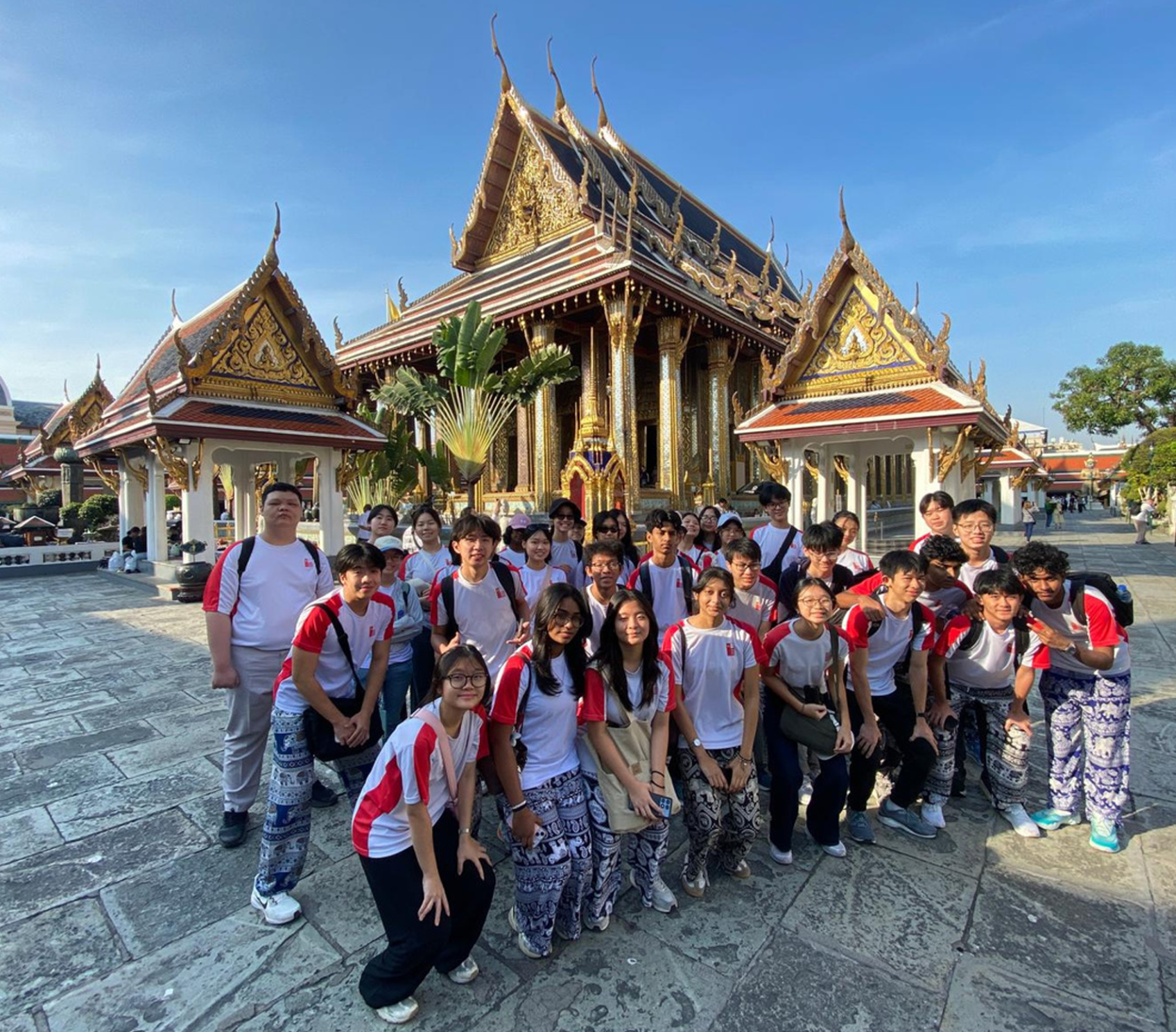 Group in matching red-and-white shirts posing in front of an ornate golden temple under blue sky