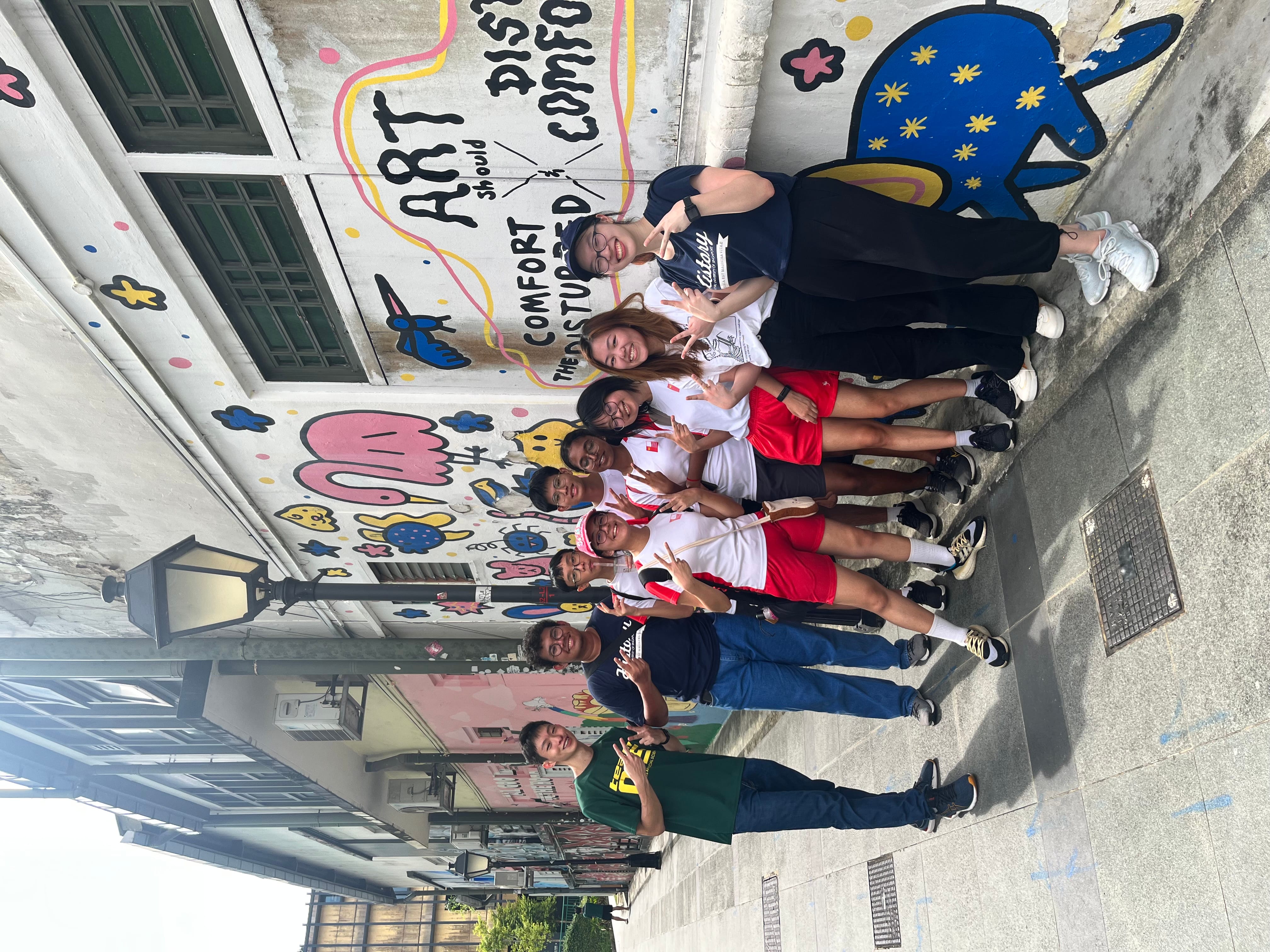 Group of eight posing on a sidewalk beside colorful mural reading ART should comfort the disturbed.
