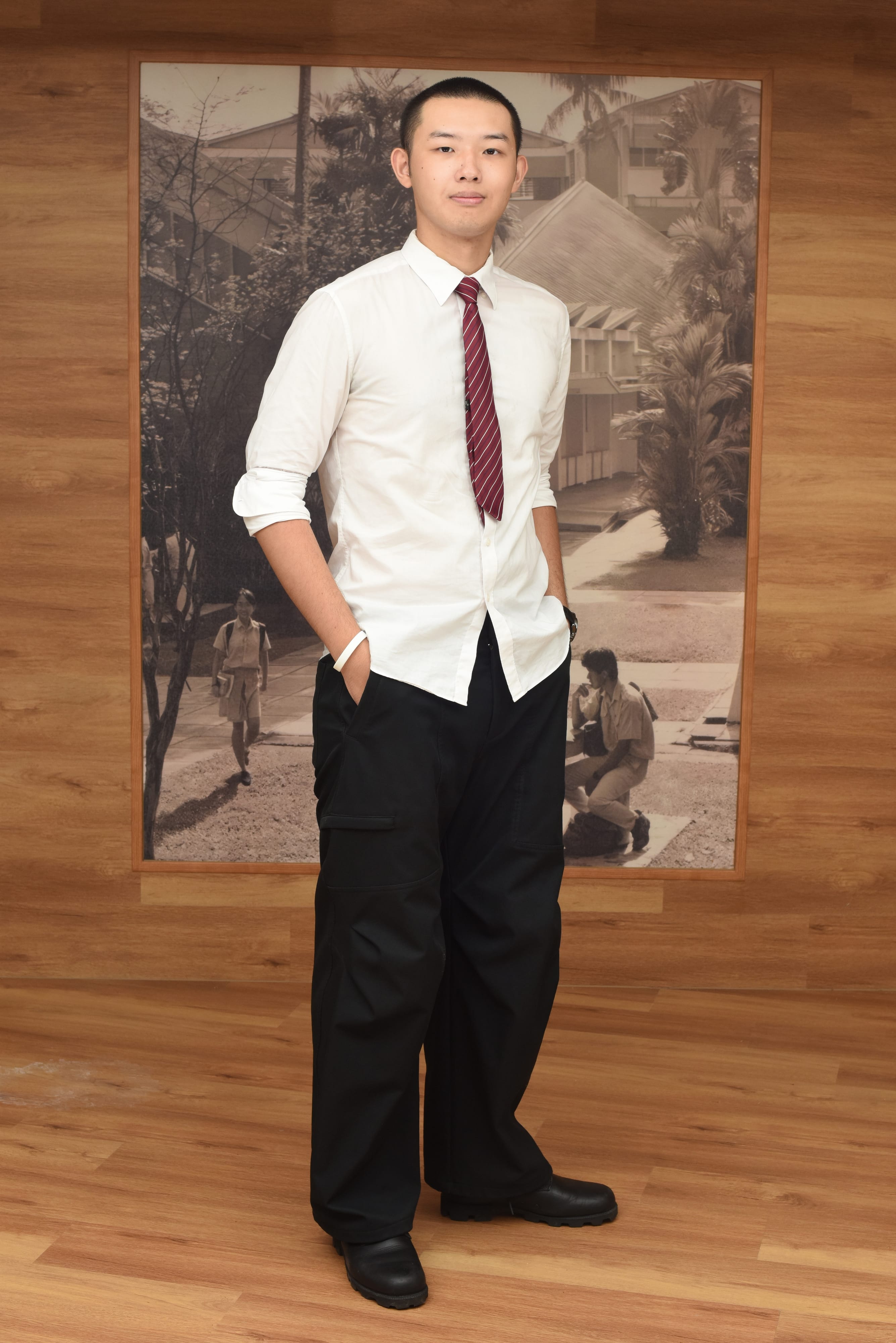 Young man in white shirt, red tie, and black pants stands on wood floor before a sepia-toned suburban photo backdrop.