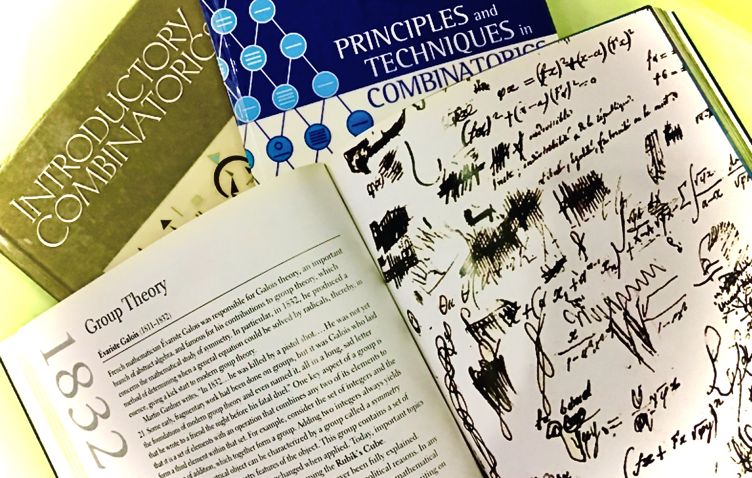 Three math books on combinatorics and group theory alongside a notebook filled with handwritten equations and scribbles.