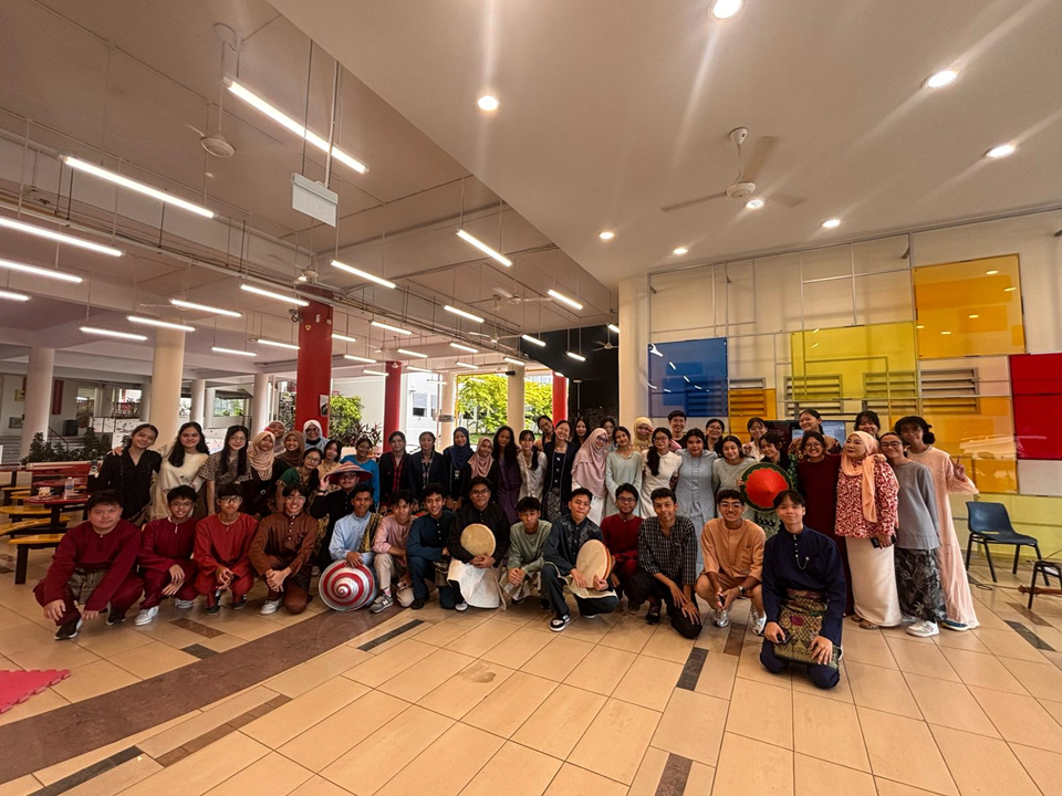 Large group of young people in traditional Southeast Asian attire posing together inside a bright indoor hall.