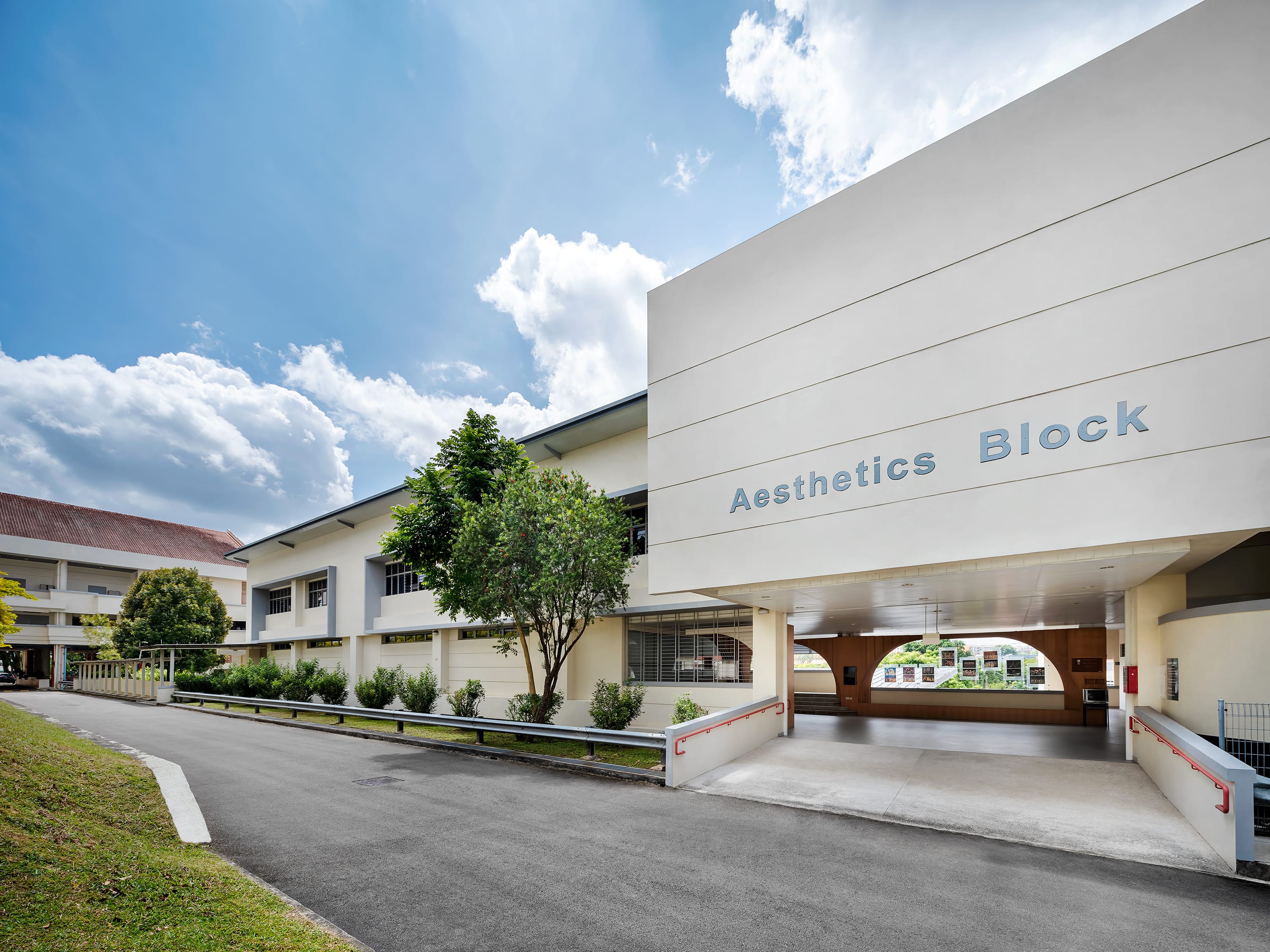 White school building with Aesthetics Block sign, driveway and trees under a blue sky with clouds.