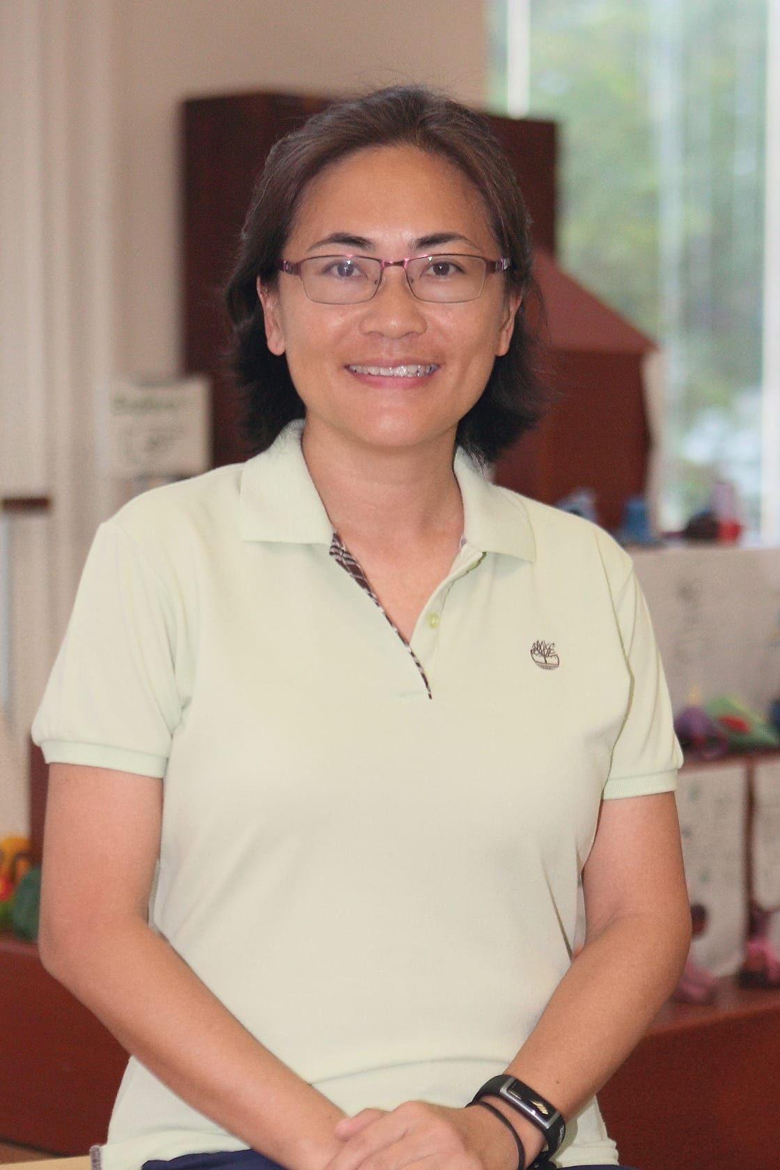 A smiling woman with glasses and braces wearing a light green Timberland polo shirt indoors.
