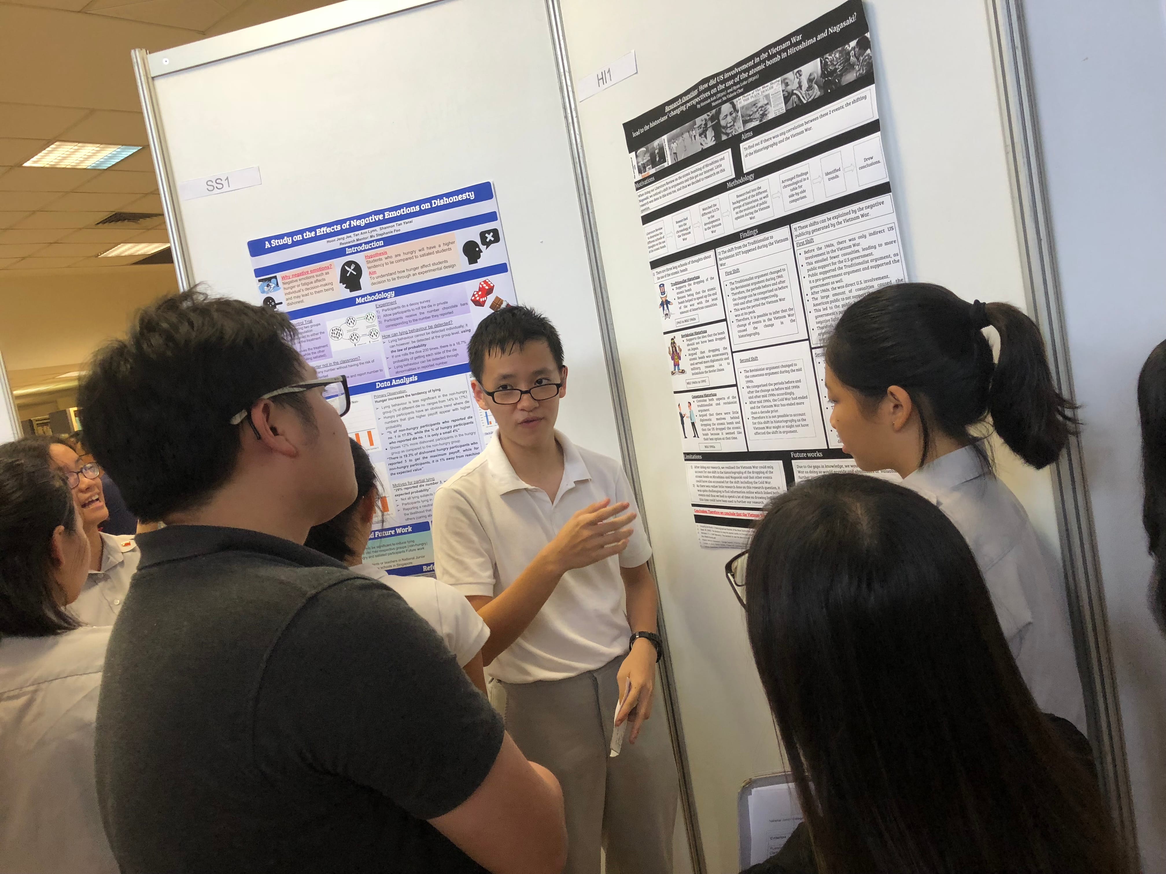 A student presents a research poster on negative emotions and dishonesty to a small group of listeners indoors.