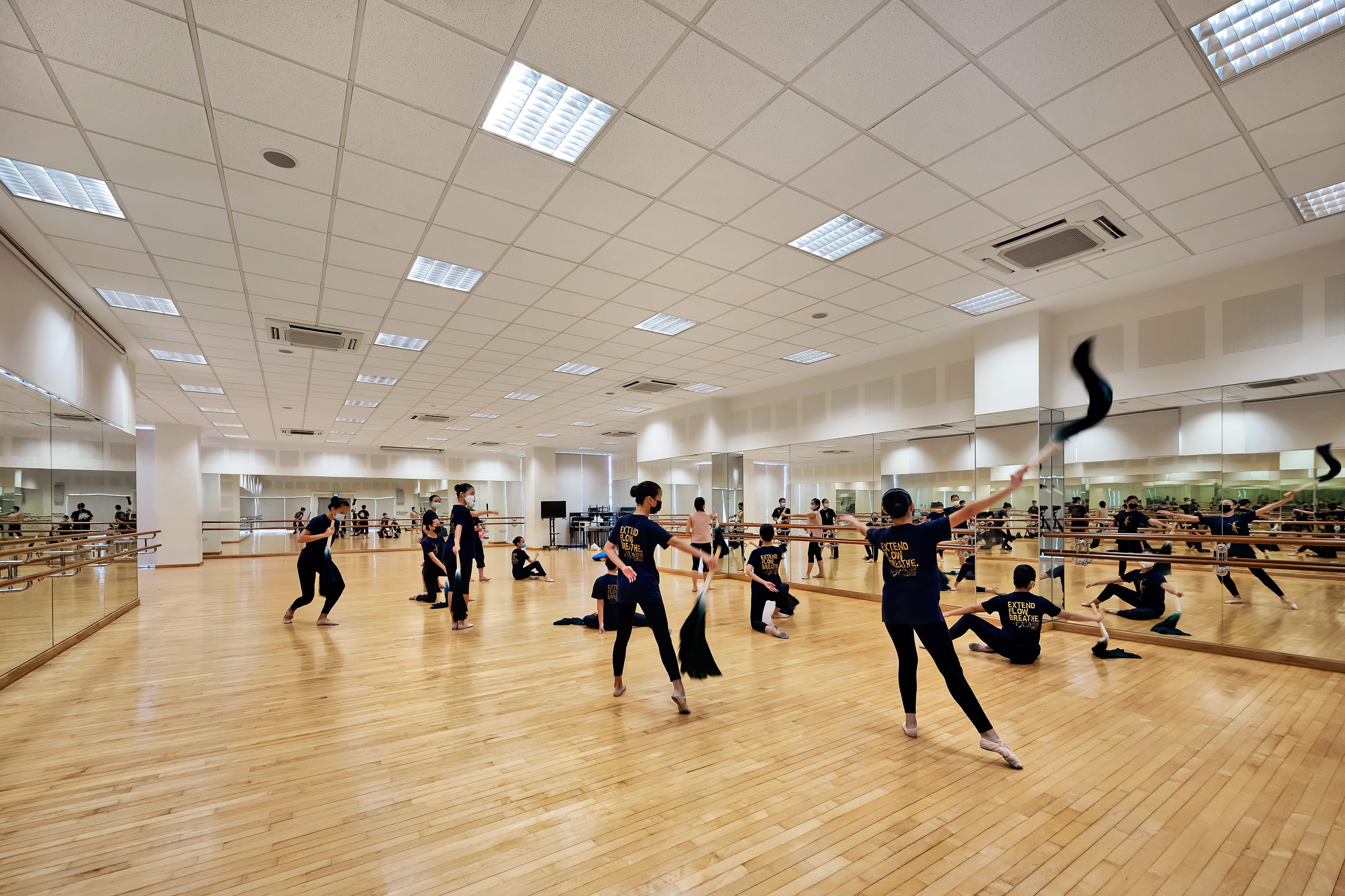 Dance studio with mirrored wall and wooden floor, dancers rehearsing while waving black cloths.