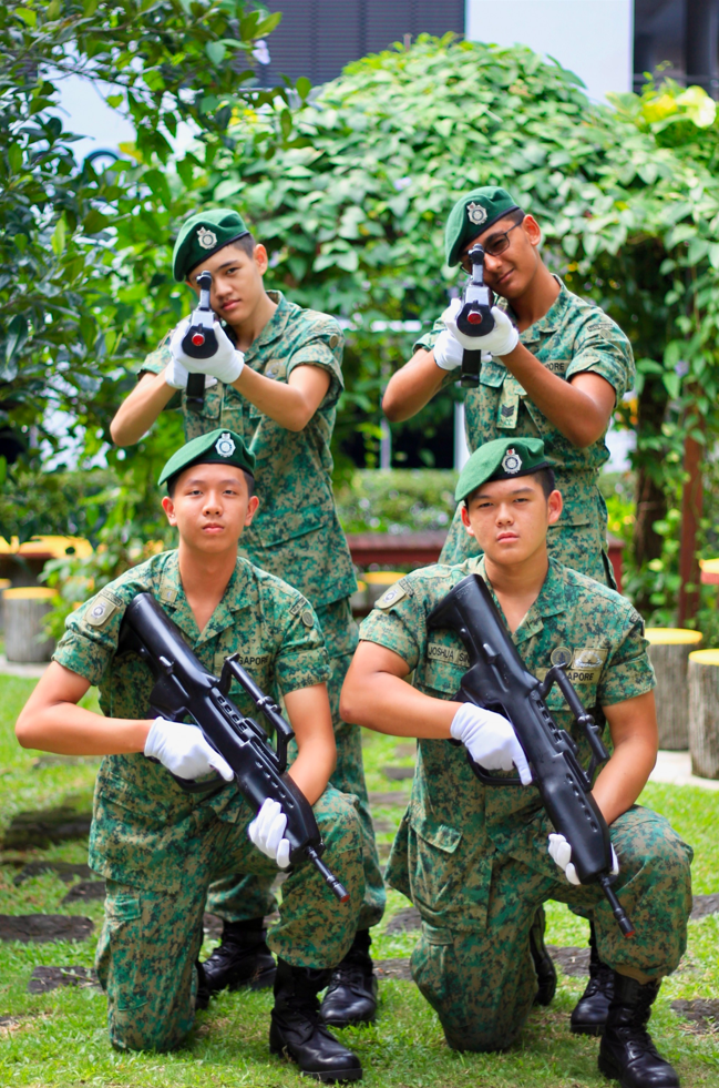 A group of NCC members in their uniforms and berets, holding a rifle prop.
