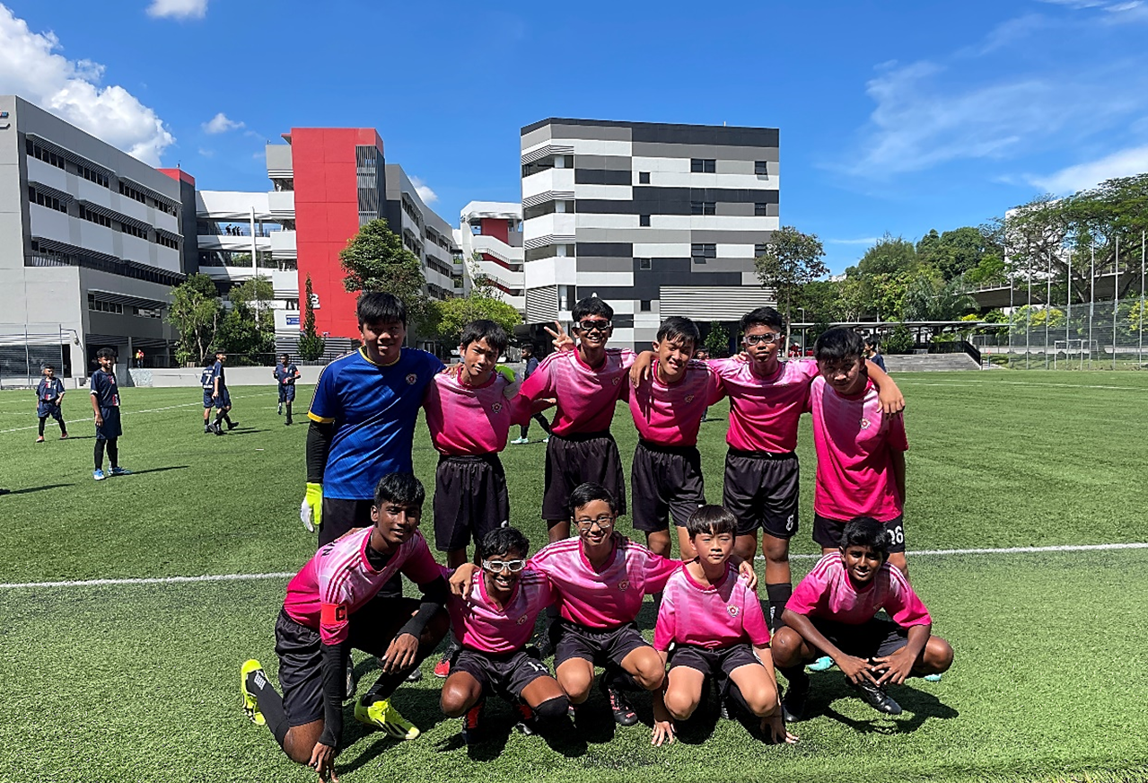 The NTSS football team in pink jerseys, posing together on a green field.