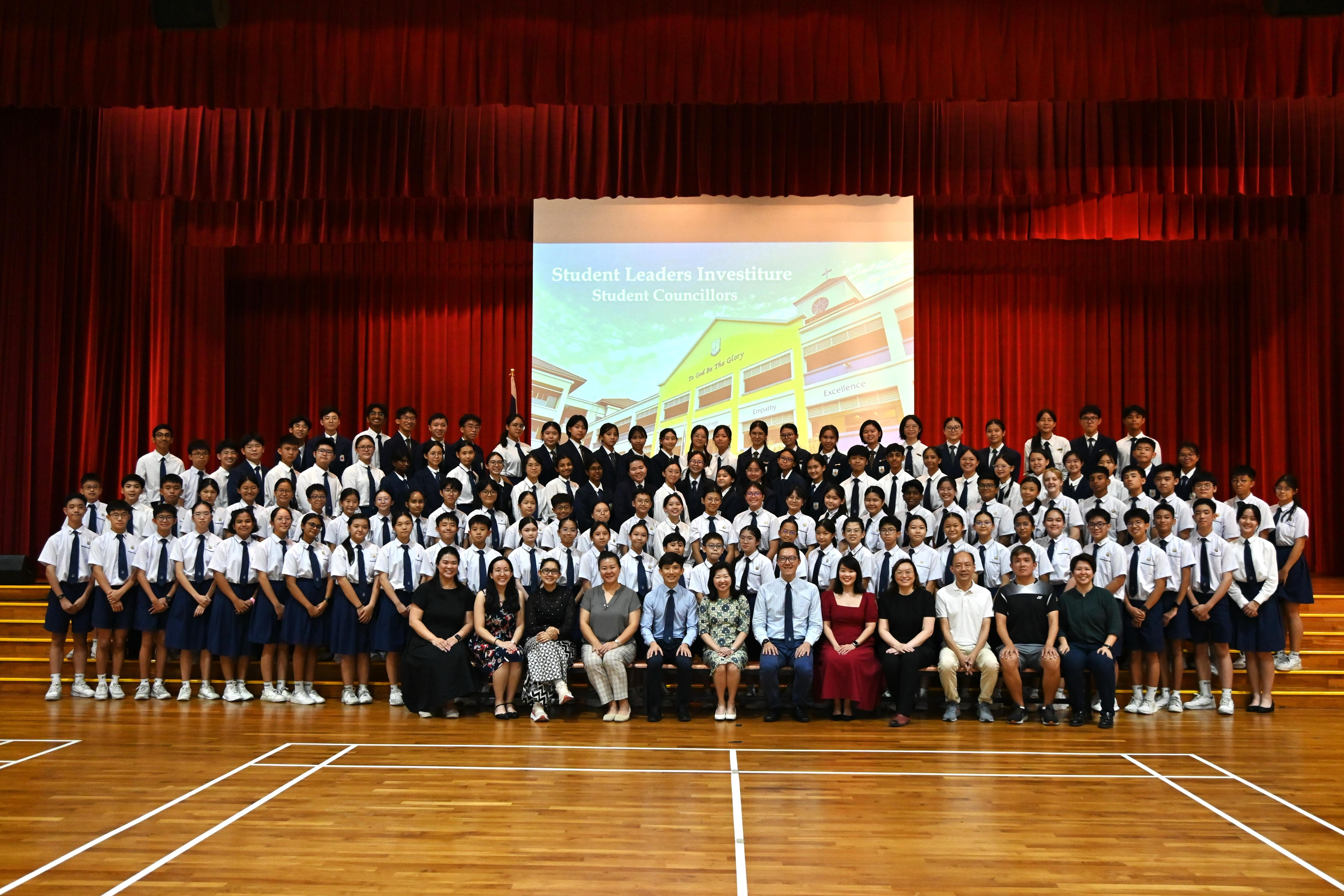 Large group of school students and teachers posing on a stage at a Student Leaders Investiture ceremony.