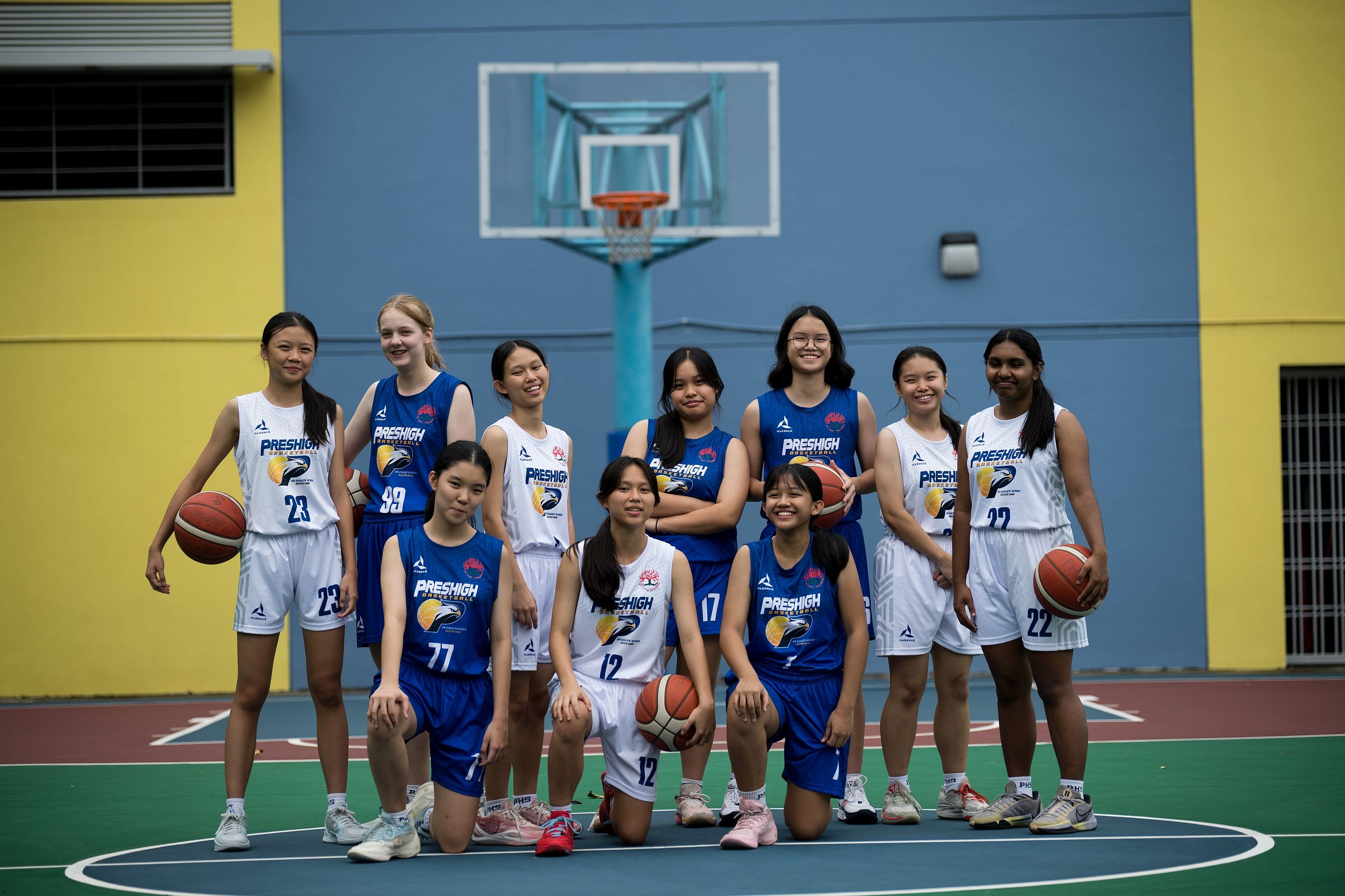 Ten girls in Preshigh basketball uniforms pose on an outdoor court with a hoop visible behind them.