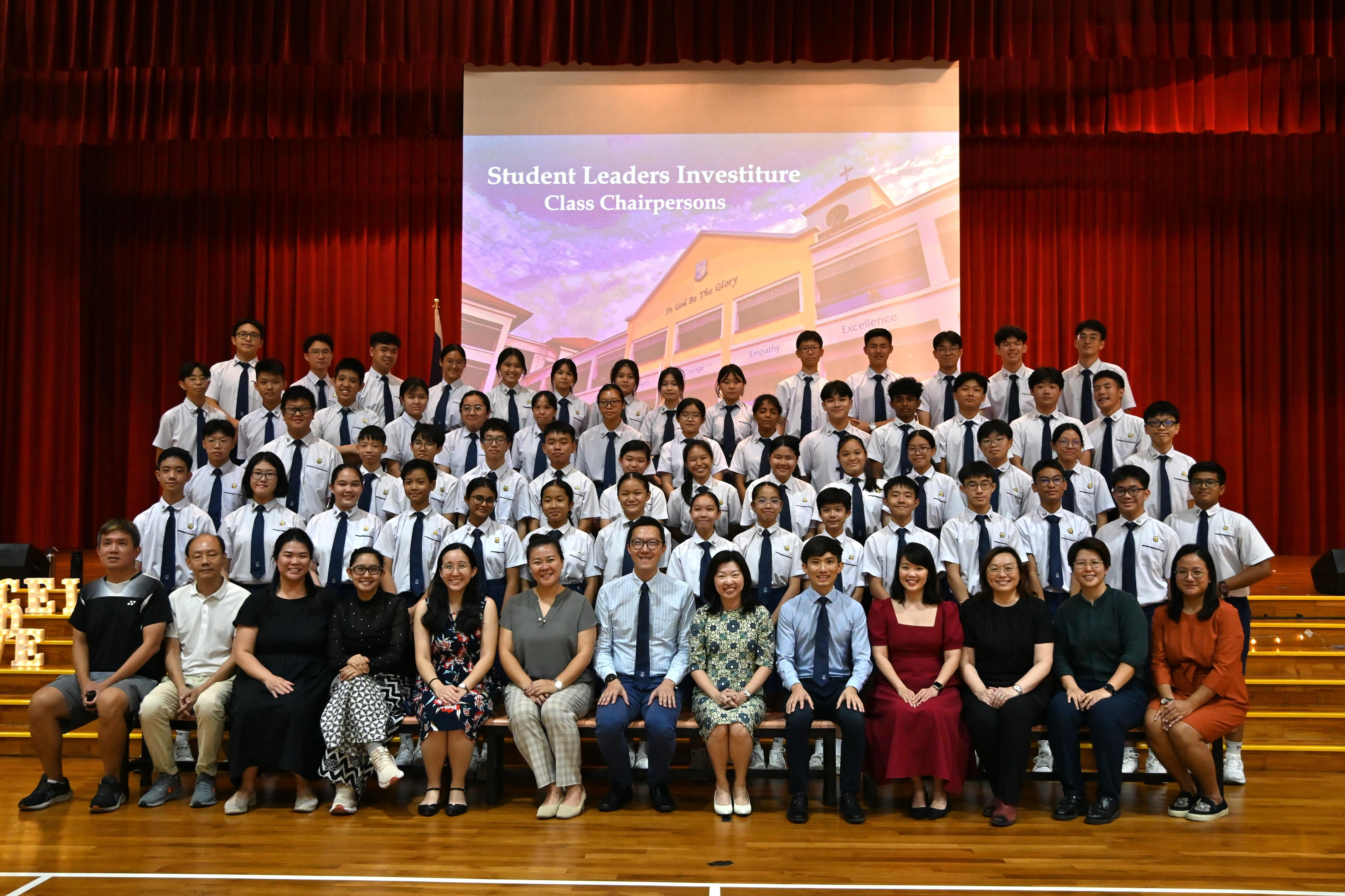 Group photo of students in white uniforms and teachers at a Student Leaders Investiture for Class Chairpersons.