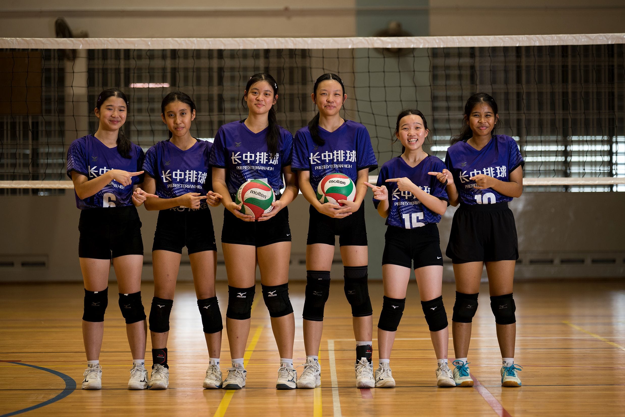 Six young female volleyball players in purple Presbyterian High jerseys pose in front of a net holding volleyballs.