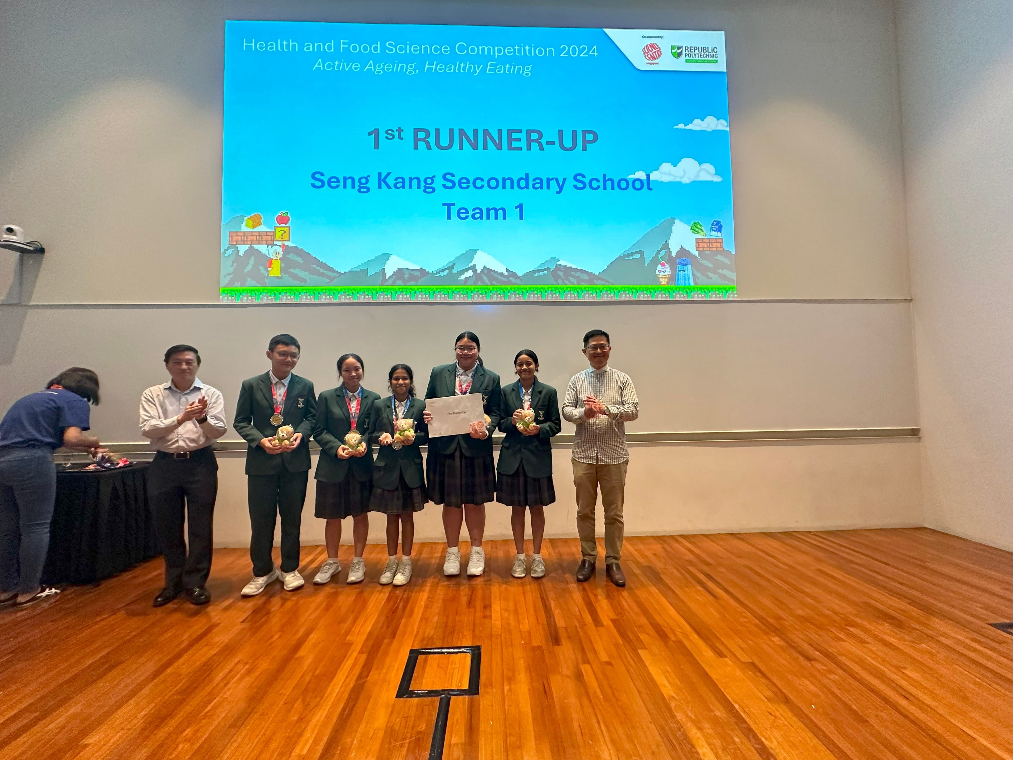 Students in uniforms pose on stage holding medals and a certificate as 1st Runner-Up at Health and Food Science Competition 2024.