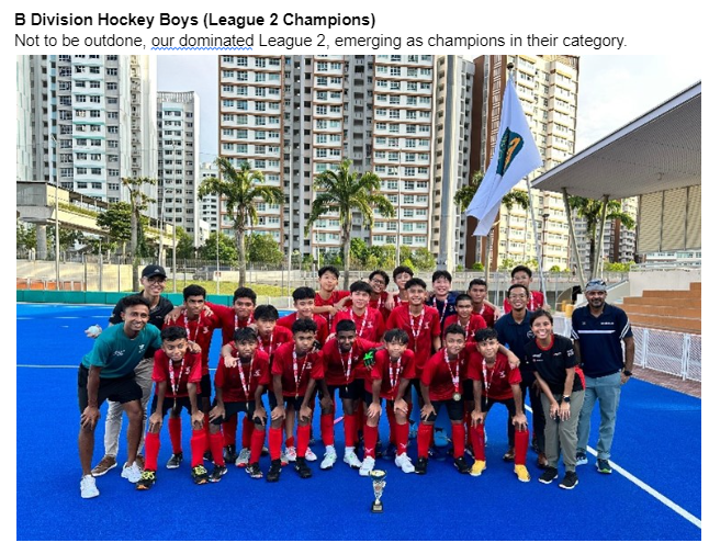 Boys hockey team in red jerseys posing with a trophy and medals on a blue turf field with buildings behind.