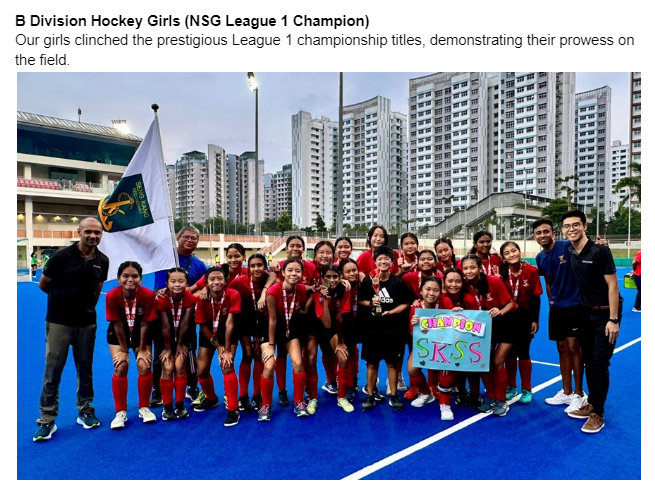 Girls hockey team in red uniforms posing with medals, a flag, and a Champion sign on a blue field.