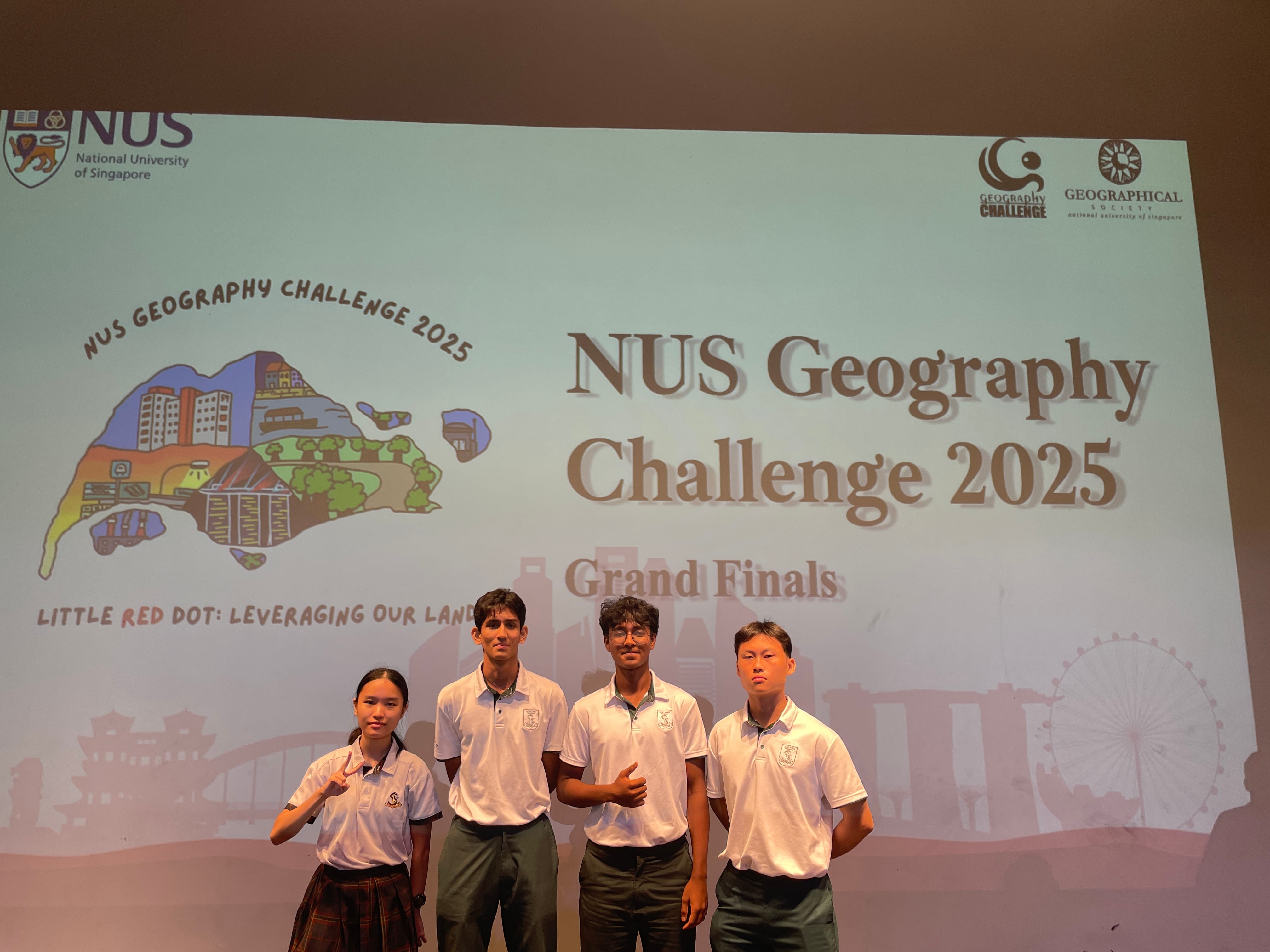 Four students in school uniforms stand before a projected screen reading NUS Geography Challenge 2025 Grand Finals.