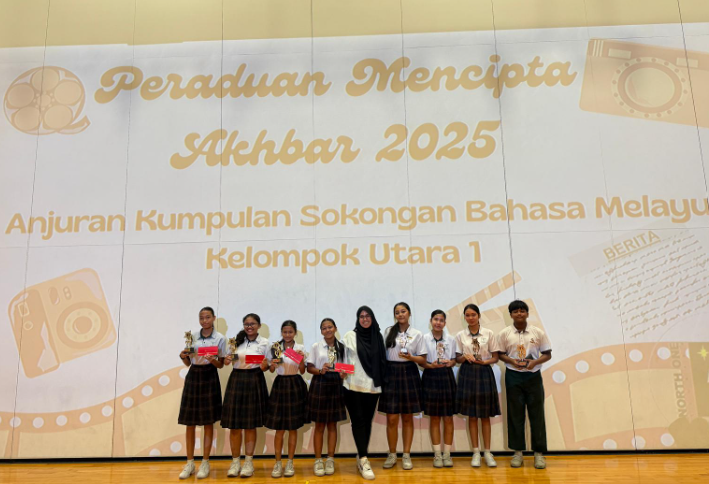 Eight students holding trophies and certificates stand in front of a Peraduan Mencipta Akhbar 2025 banner.