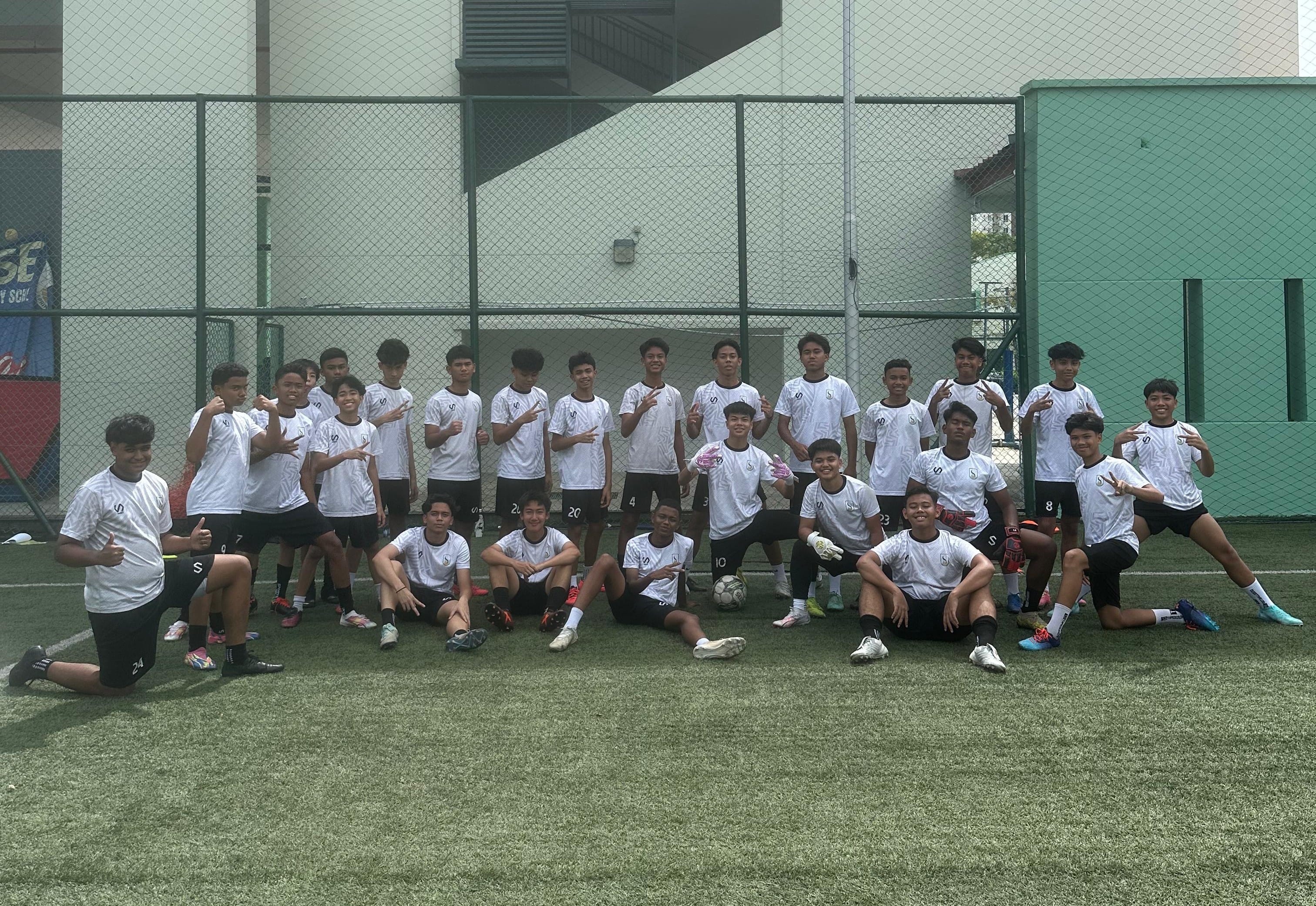 A youth football team in white and black uniforms poses together on an outdoor artificial turf pitch.