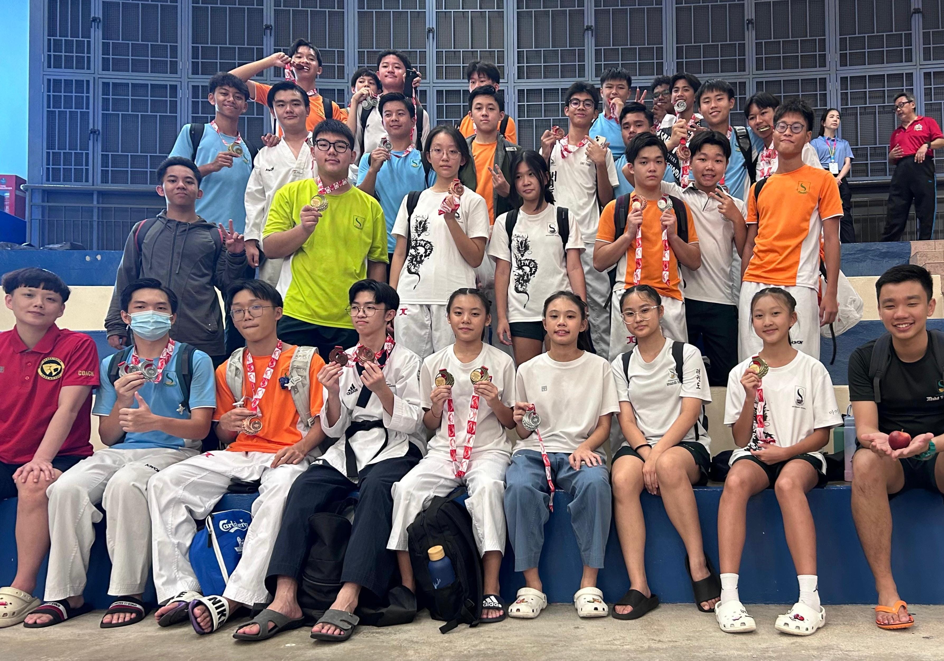 A large group of young athletes posing together on bleachers, many holding up medals and smiling.
