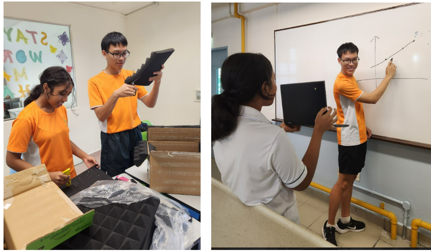 Two students in orange shirts unpack boxes, and a boy draws on a whiteboard while a girl holds a monitor.
