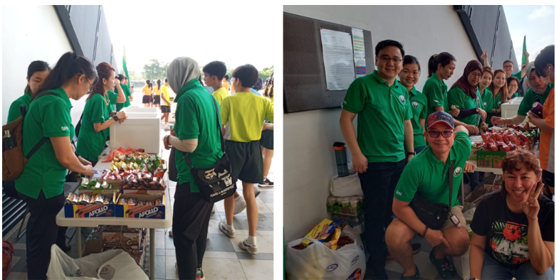 People in green shirts distribute snacks and food items at an outdoor event booth.