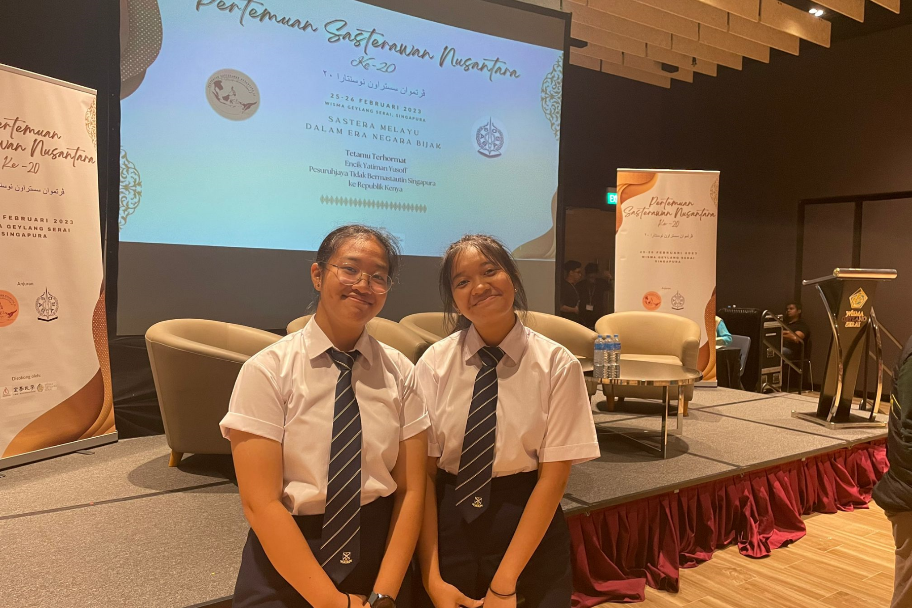 2 students standing in front of a stage at a live seminar.