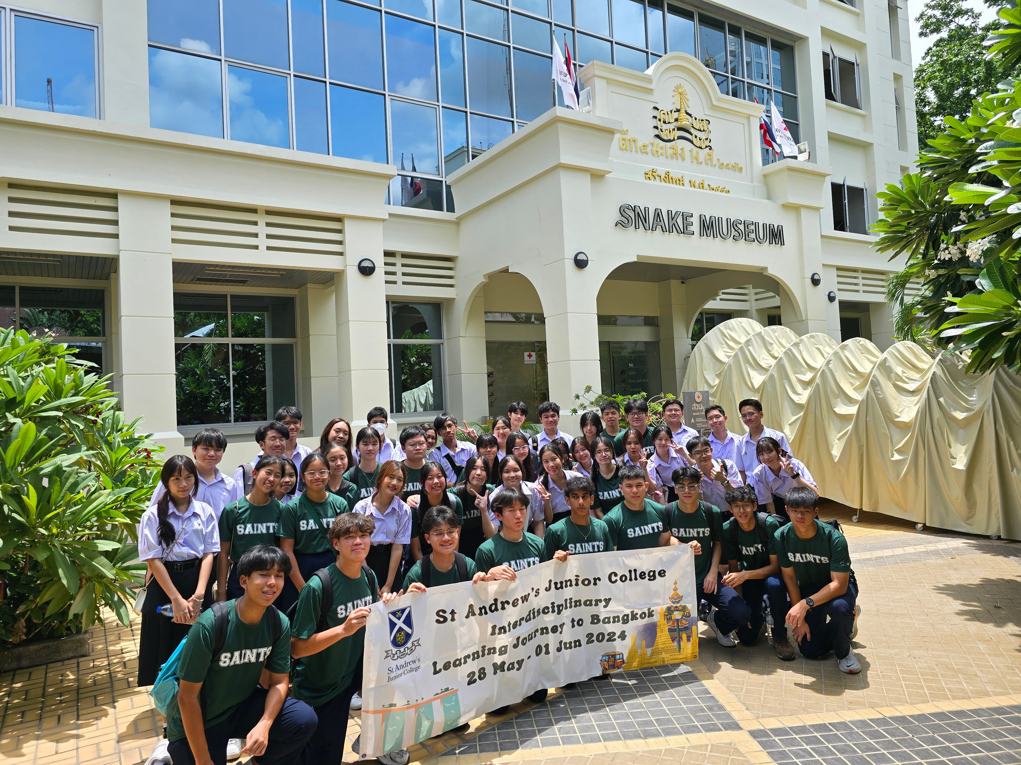 Students from St Andrew's Junior College pose for a group photo in front of the Snake Museum in Bangkok, holding a banner that reads 'St Andrew's Junior College Interdisciplinary Learning Journey to Bangkok, 28 May – 01 Jun 2024'.