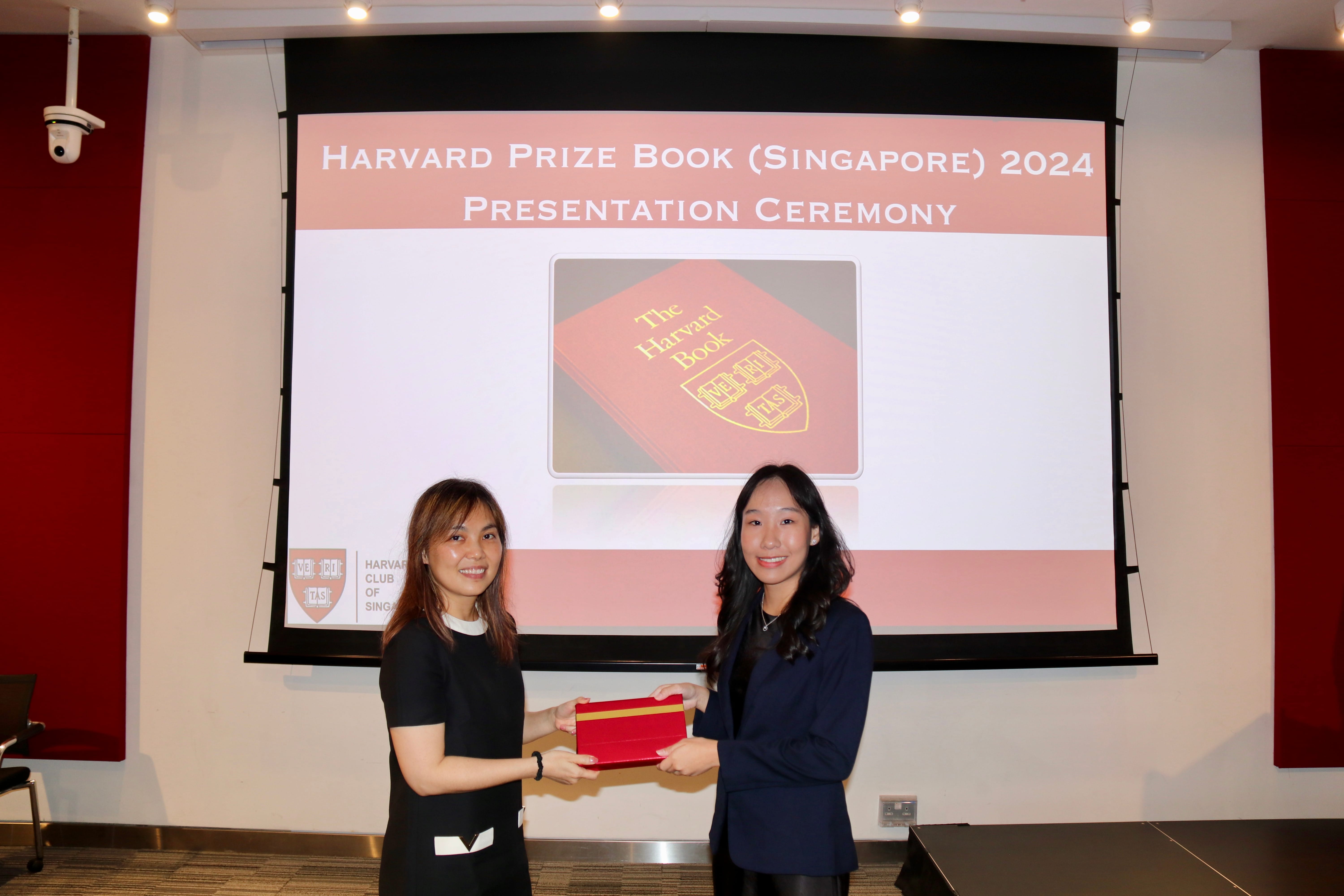 Two women hold a red book together at the Harvard Prize Book Singapore 2024 Presentation Ceremony.