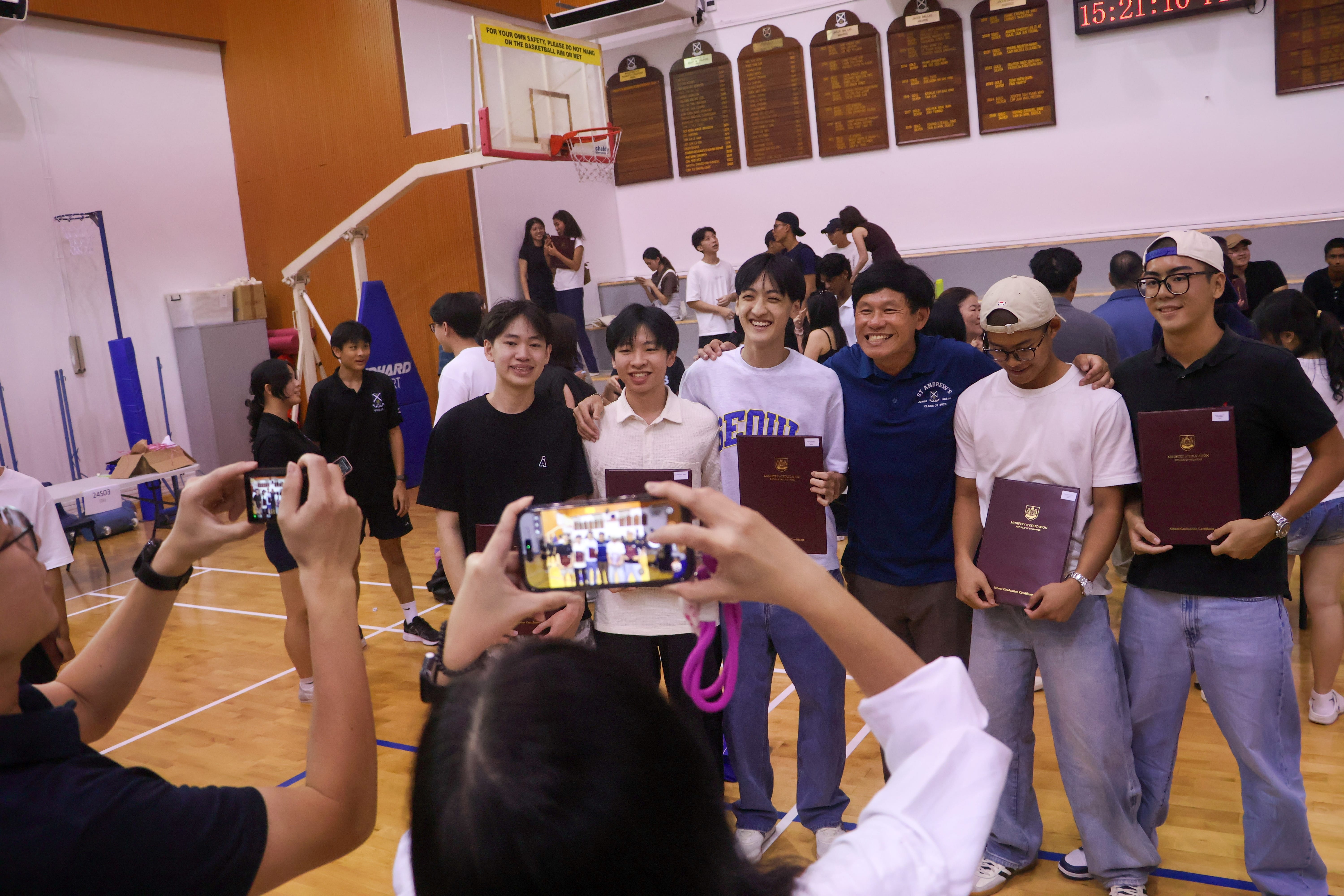 Five happy graduates posing for a photo with their teacher.