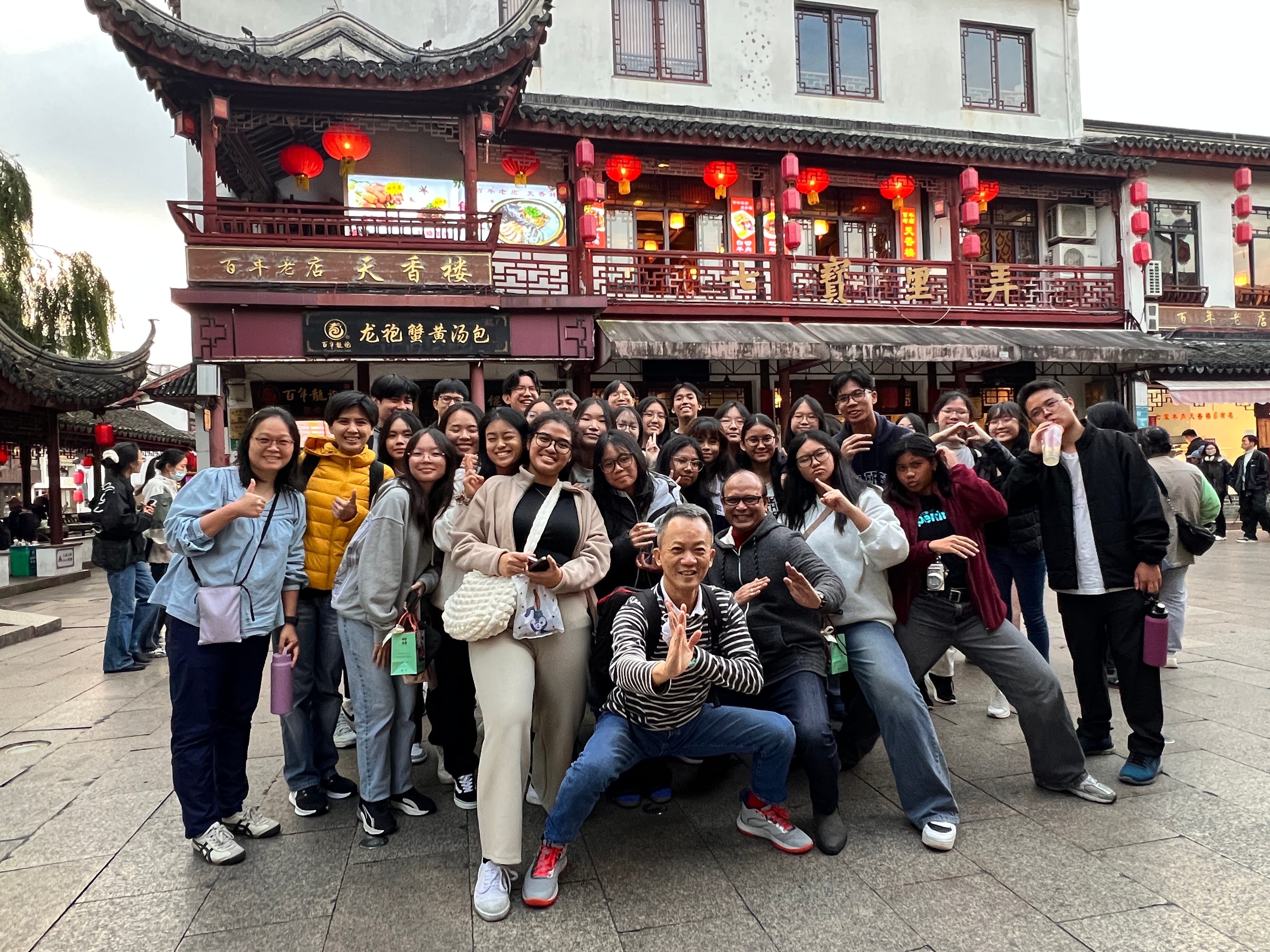 A large group of people posing in front of a traditional Chinese building decorated with red lanterns.