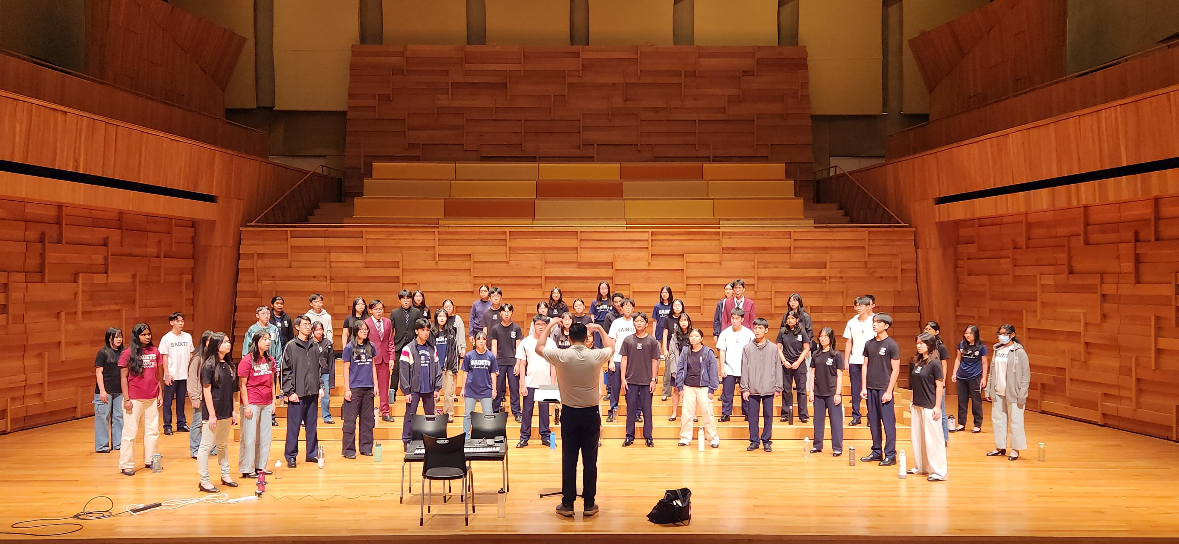 The Saints Chorale rehearsing on stage with their conductor