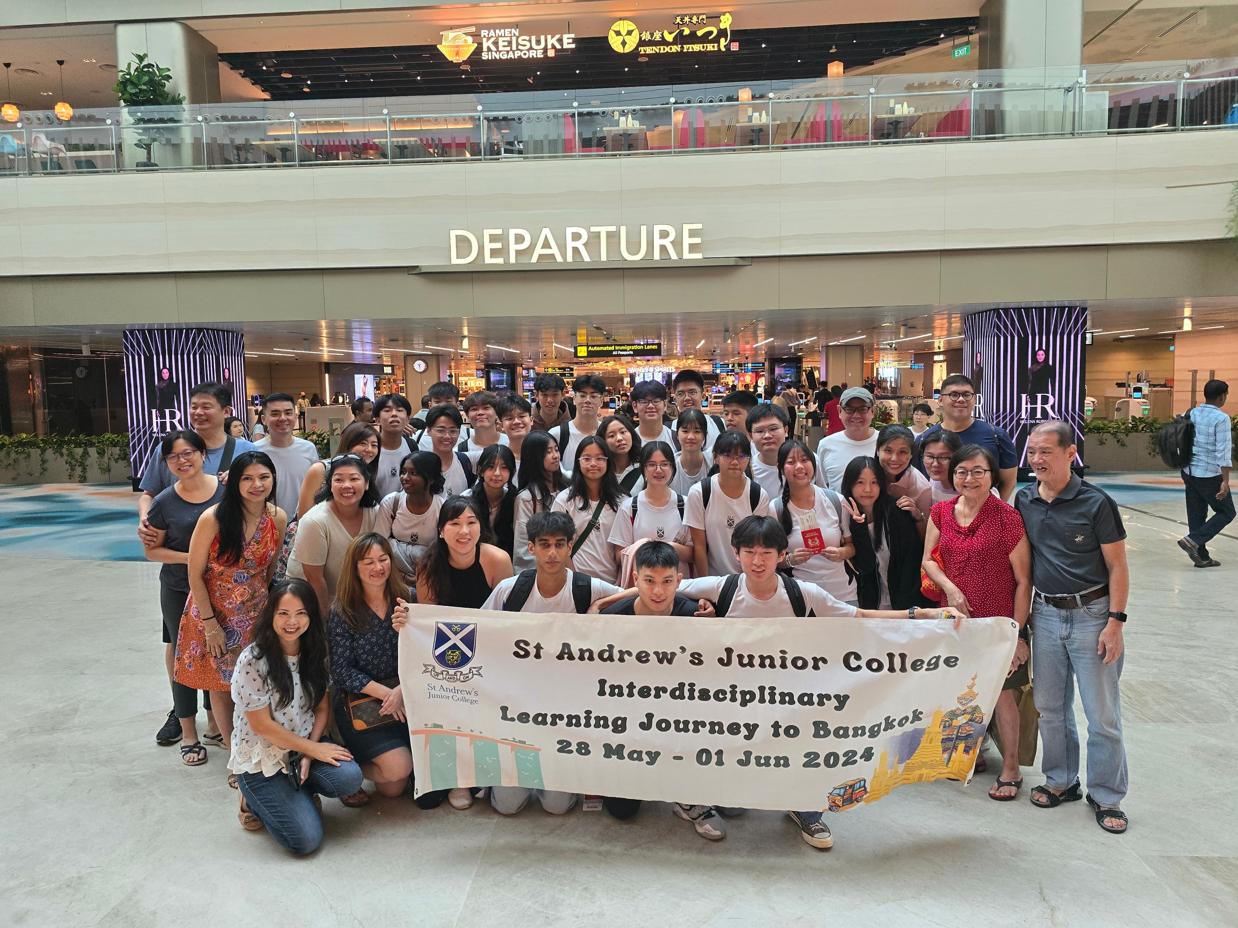 Large group poses at airport departure hall holding a St Andrew's Junior College Bangkok Learning Journey banner, May 2024.