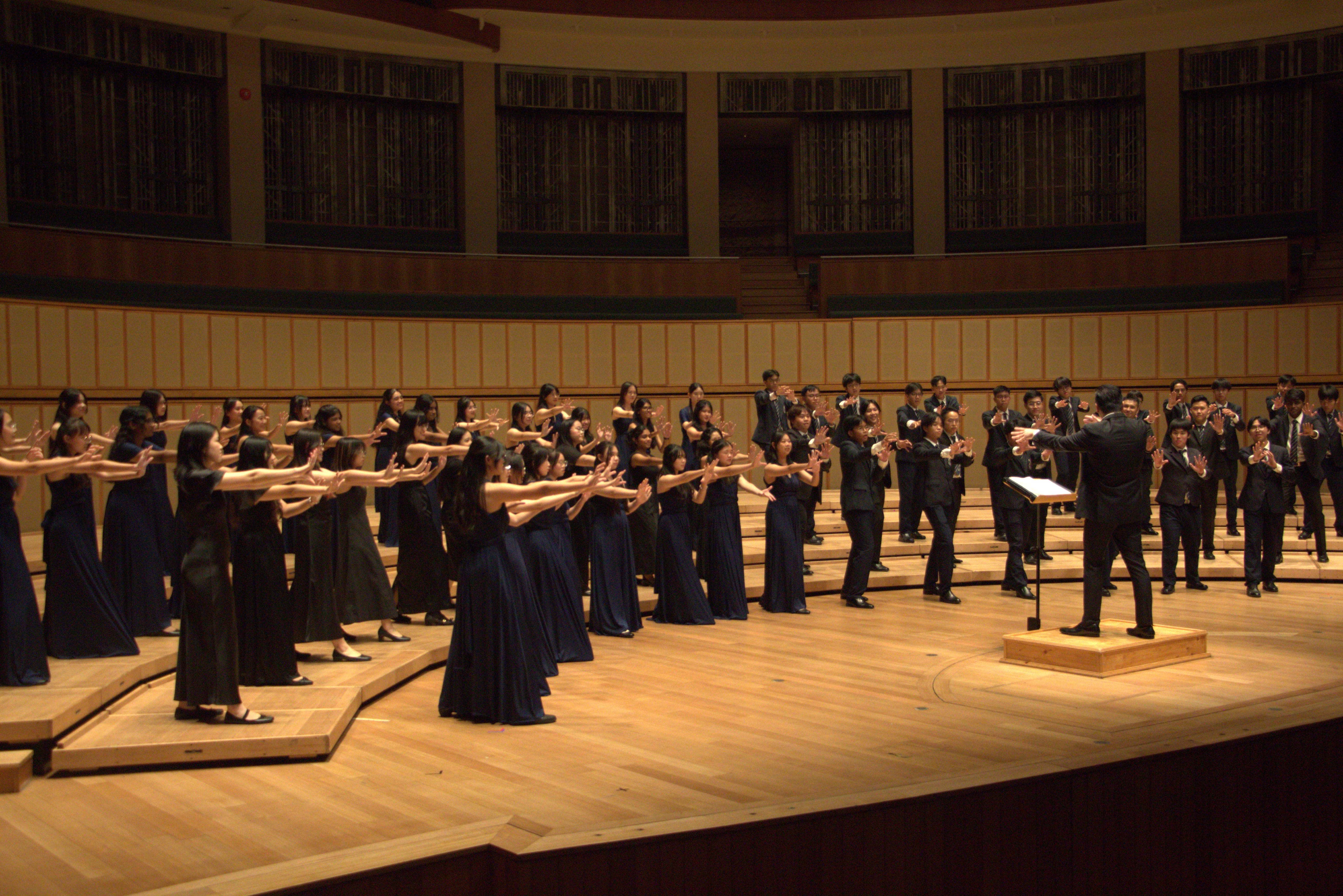 The Saints Chorale in the middle of a performance on stage with their conductor.