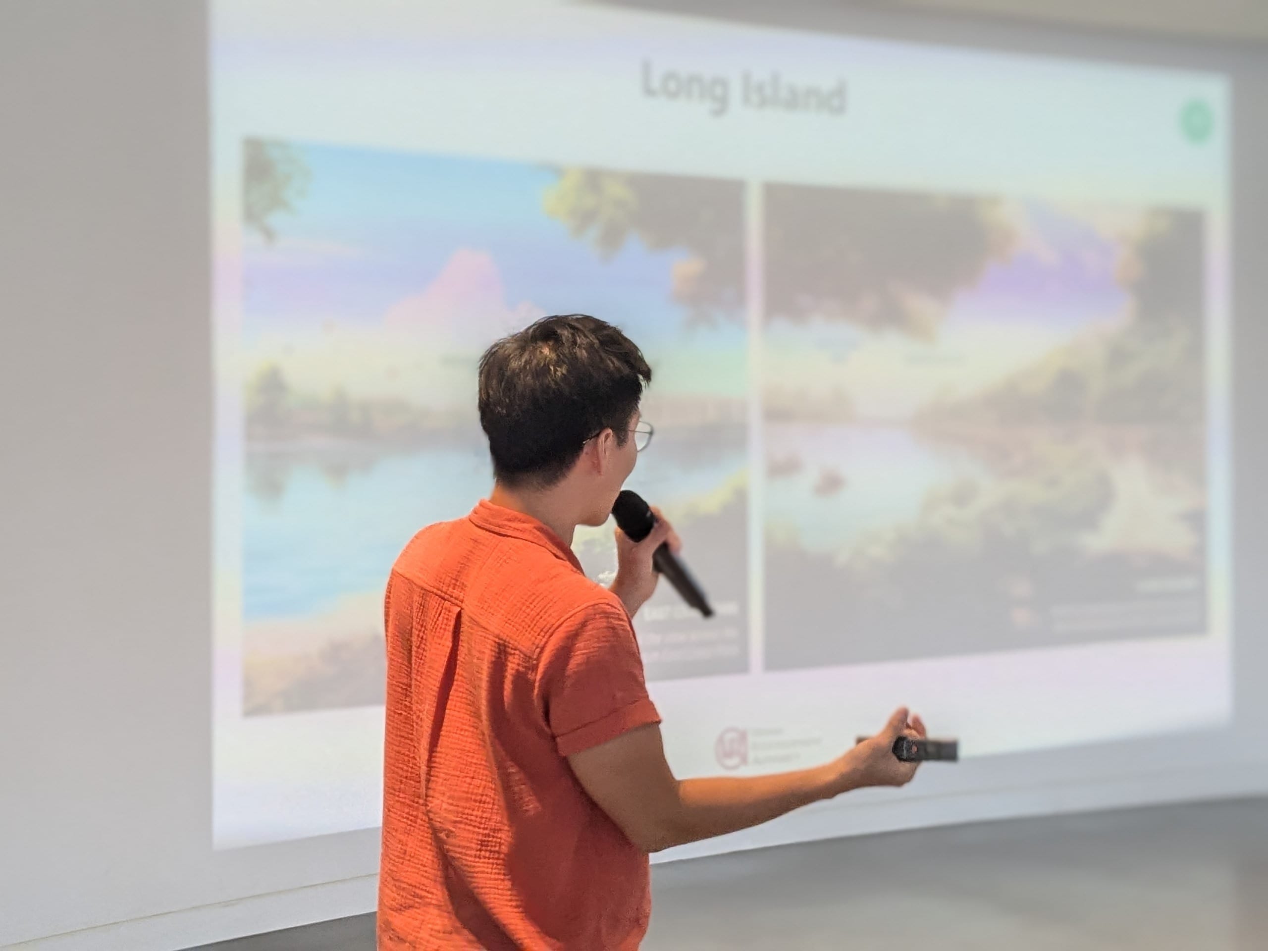 Person in an orange shirt holding a microphone, presenting a slideshow titled Long Island with landscape paintings.
