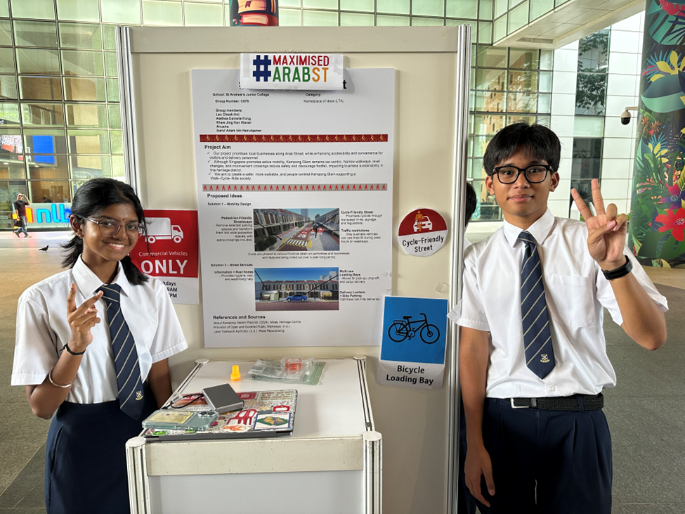 Two St Andrew's Junior College students pose with peace signs beside their "#MaximisedArabSt" project board, which proposes mobility and street improvements for the Kampong Glam/Arab Street area.