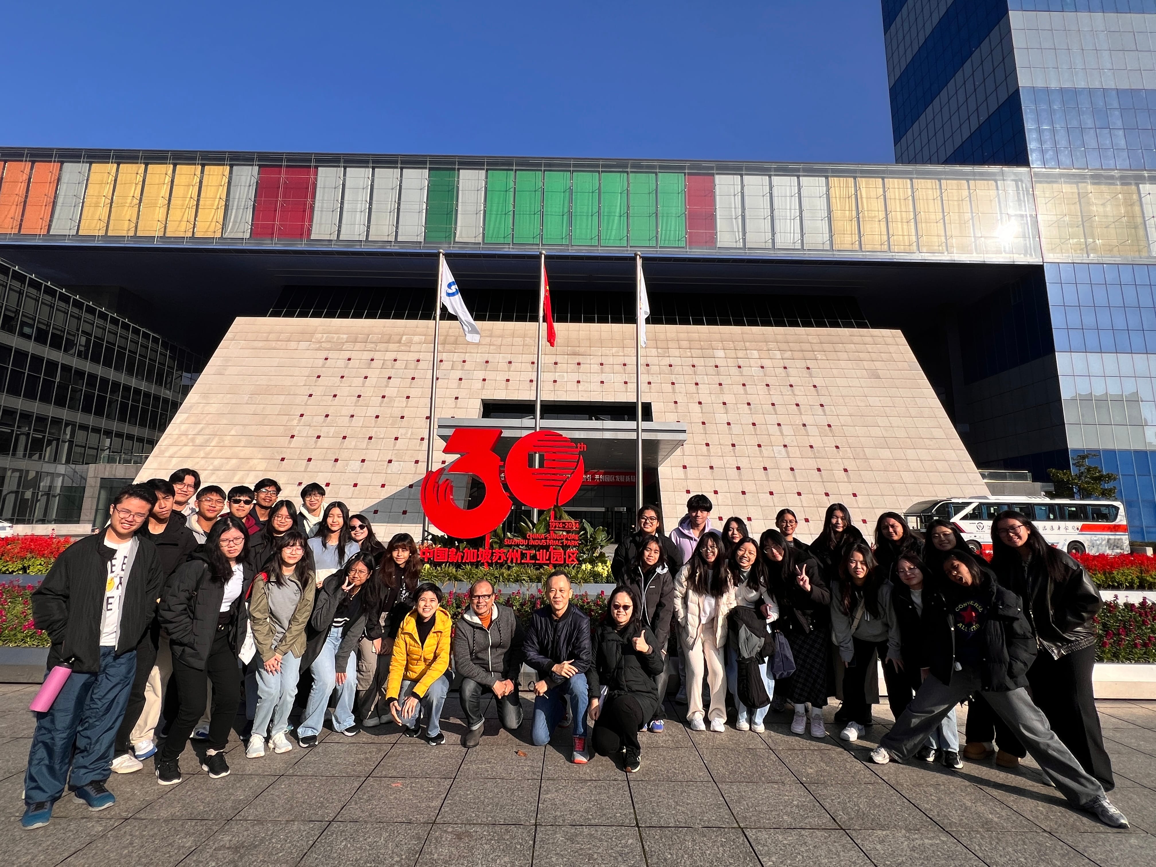 Large group of people posing in front of Suzhou Industrial Park building with a red 30th anniversary sign.